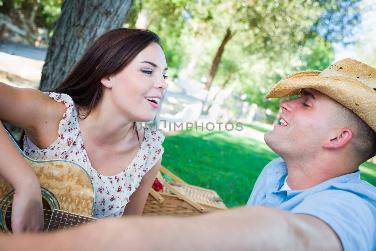 Young Adult Girl Playing Guitar with Boyfriend In The Park.