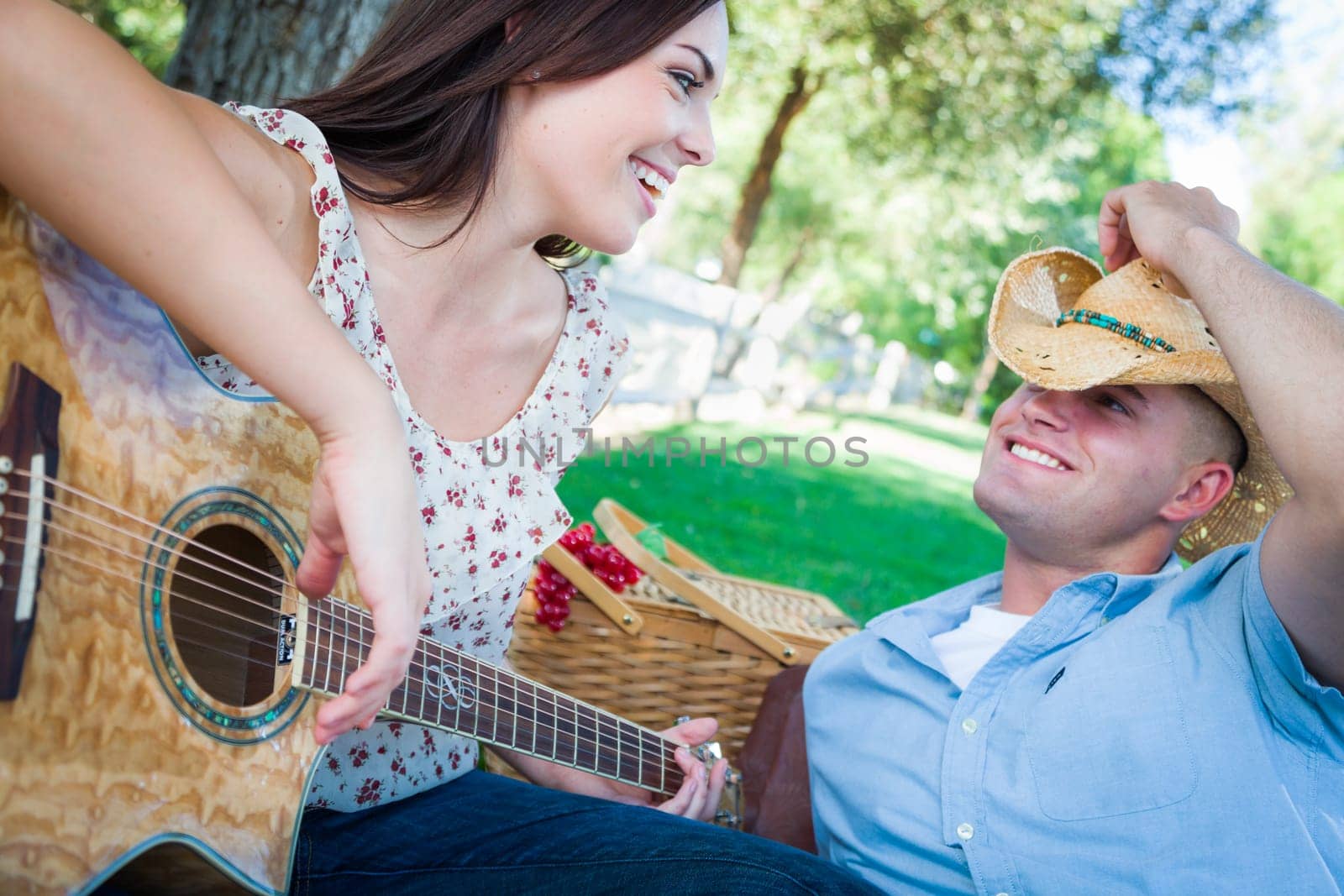 Young Adult Girl Playing Guitar with Boyfriend In The Park.