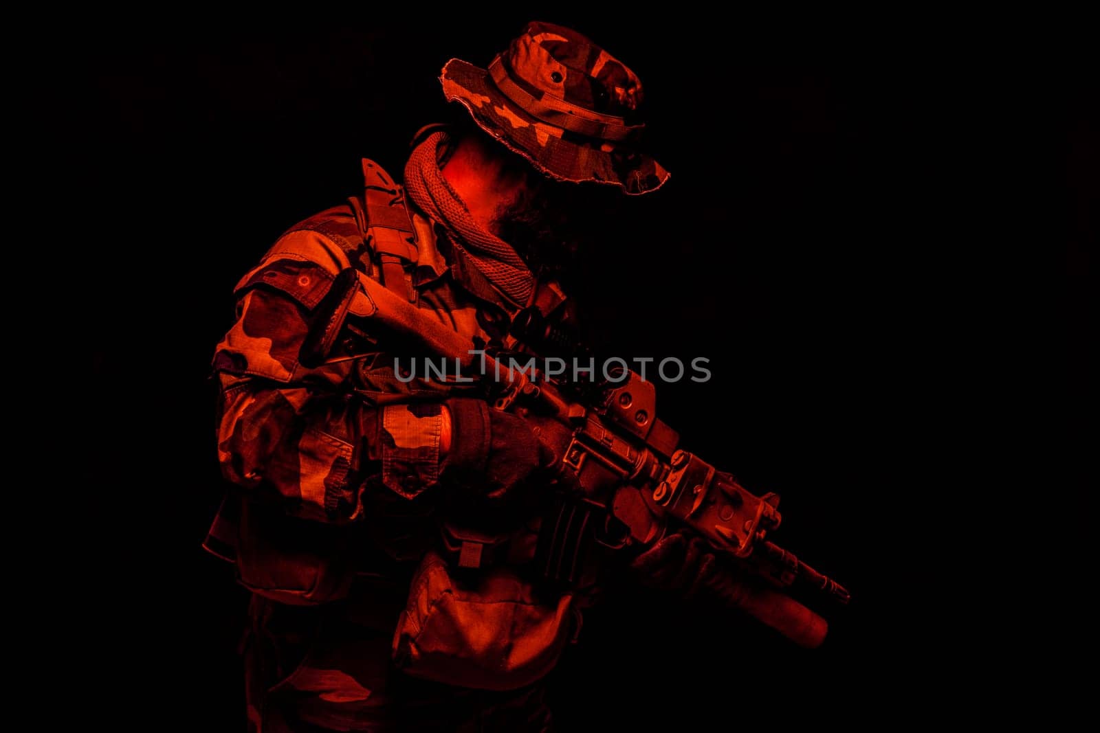 Commando shooter, army special forces rifleman in battle uniform, boonie hat, ammunition in load carrier, camouflaged with paint face, armed assault rifle, half length toned colorized portrait on black background