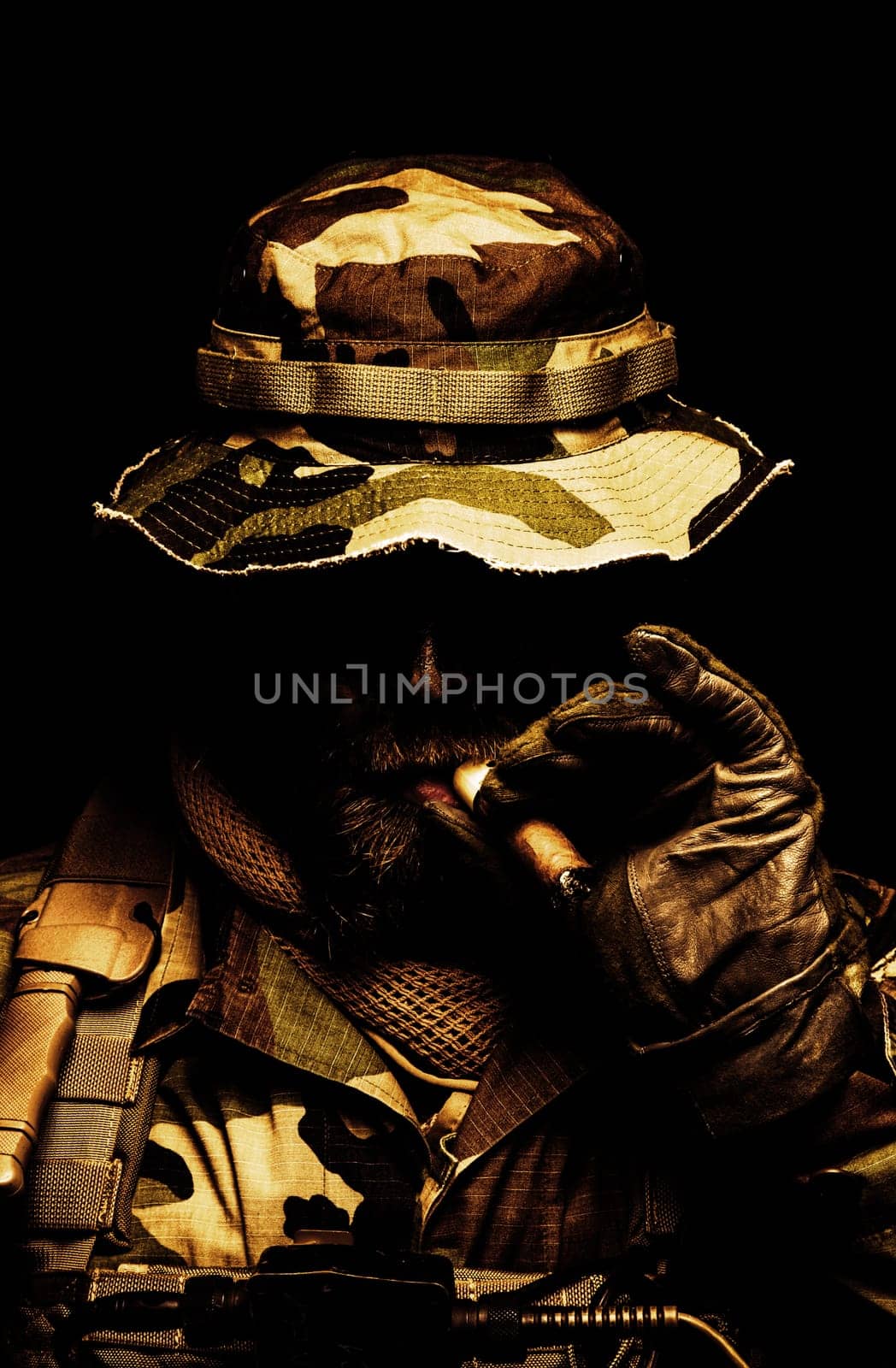 Brutal and serious commando soldier, army special forces veteran, in camouflage battle uniform, boonie hat, black paint on bearded face, combat knife in shoulder holder, smoking cigar, studio portrait toned and colorized