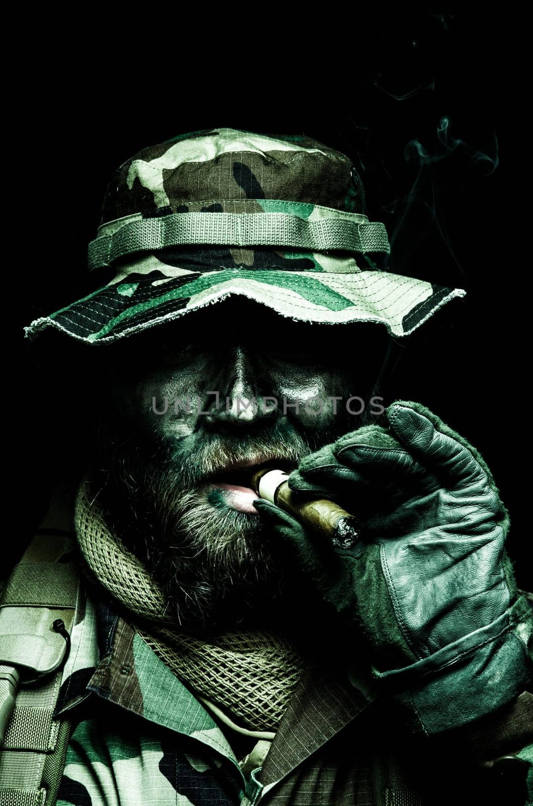 Brutal and serious commando soldier, army special forces veteran, in camouflage battle uniform, boonie hat, black paint on bearded face, combat knife in shoulder holder, smoking cigar, studio portrait toned and colorized