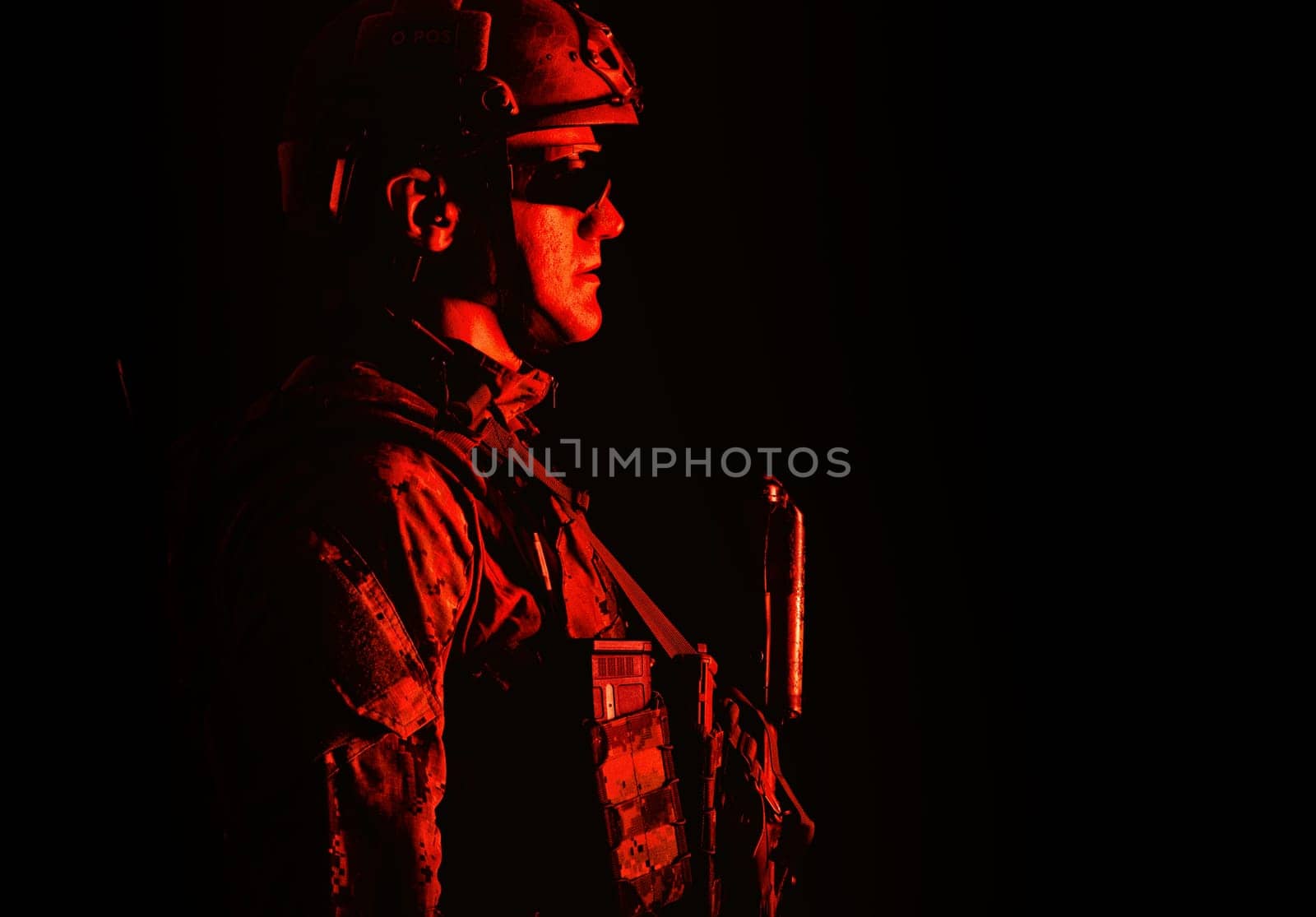 Half length low angle studio shot of special forces soldier in field uniforms with weapons, portrait on black background. Protective goggles glasses are on