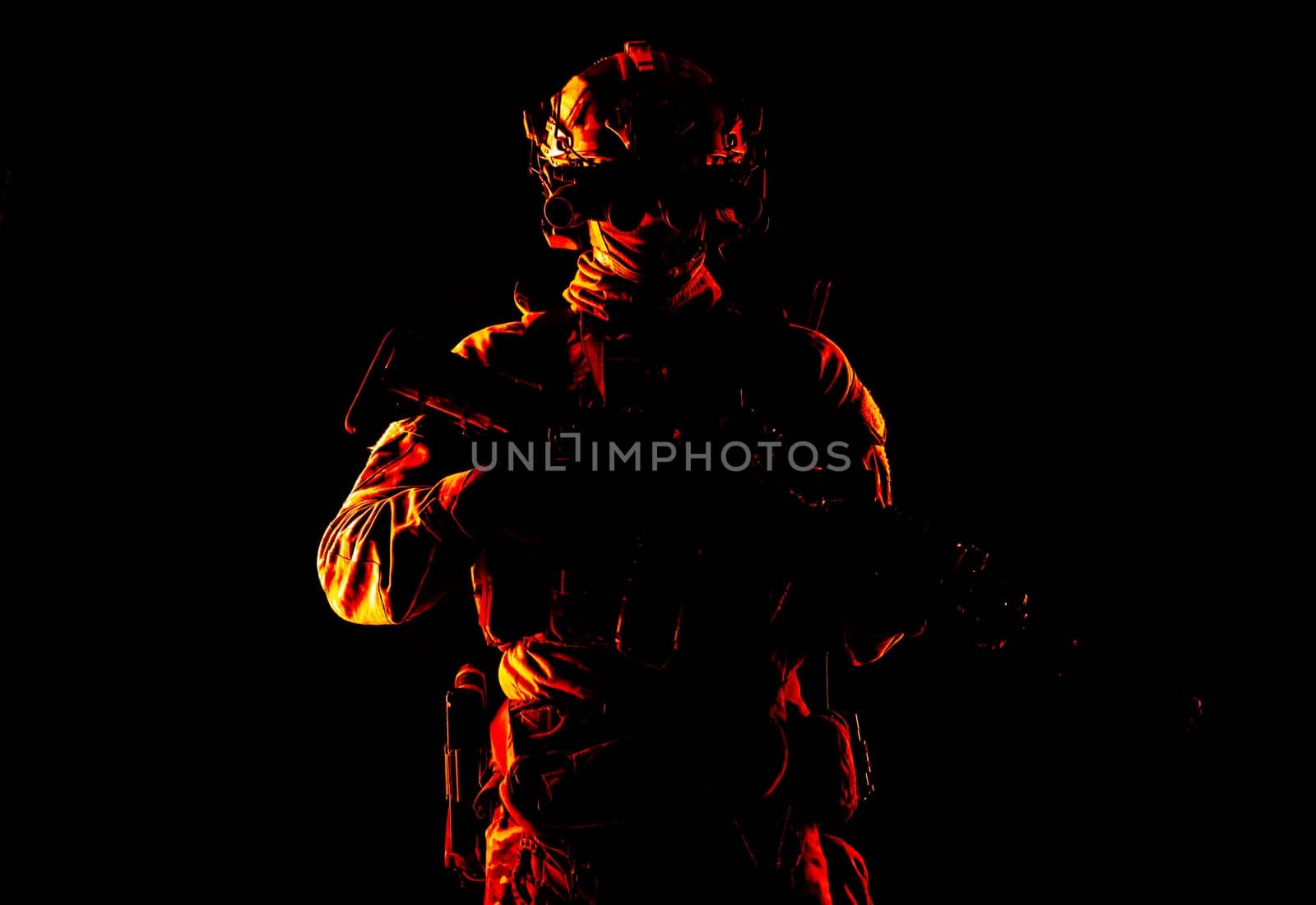 Half length, low key studio shoot of army soldier, marine infantryman in mask, camo uniform, equipped modern ammunition, armed service rifle standing in darkness with night vision device on helmet