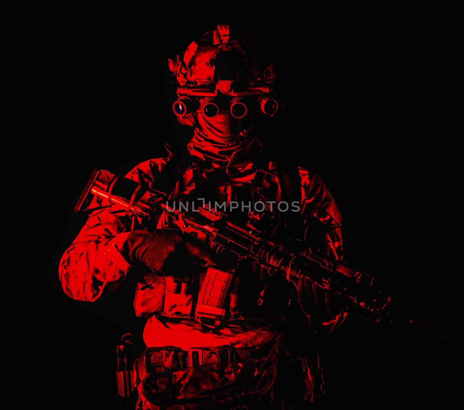 Half length, low key studio shoot of army soldier, marine infantryman in mask, camo uniform, equipped modern ammunition, armed service rifle standing in darkness with night vision device on helmet