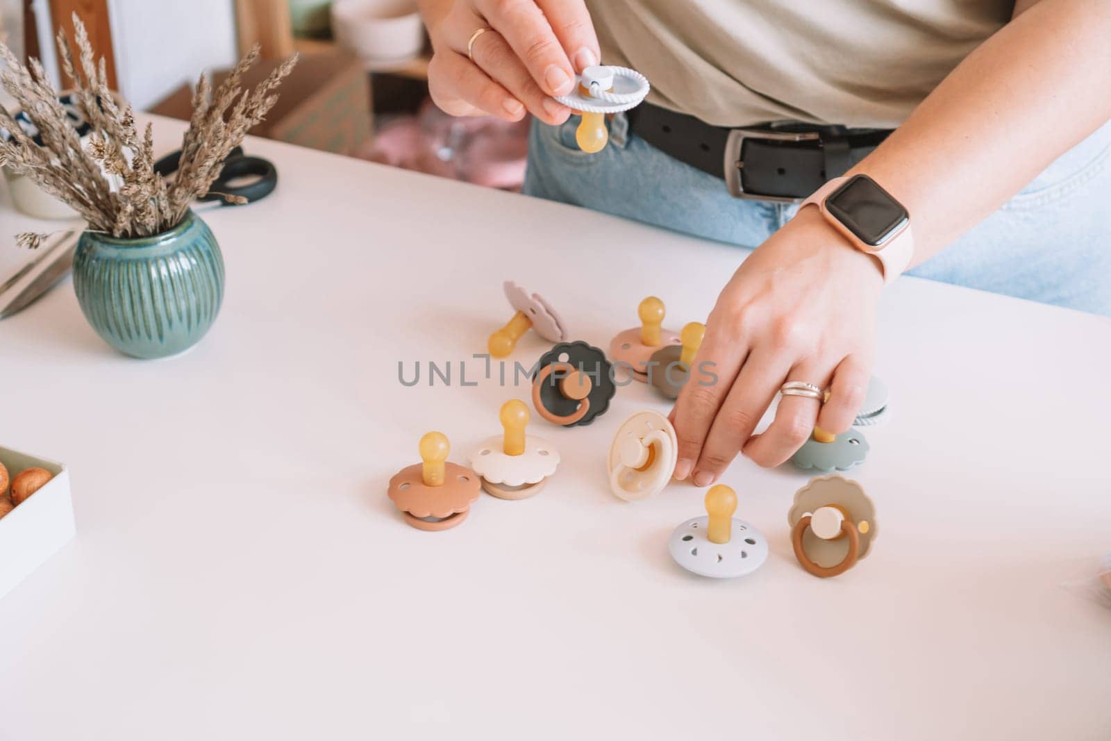 Cropped business woman hands, making and design craft silicone pacifiers for newborn babies on white desk. Small business, store. Choosing soft material for kids. Natural ecological accessories.