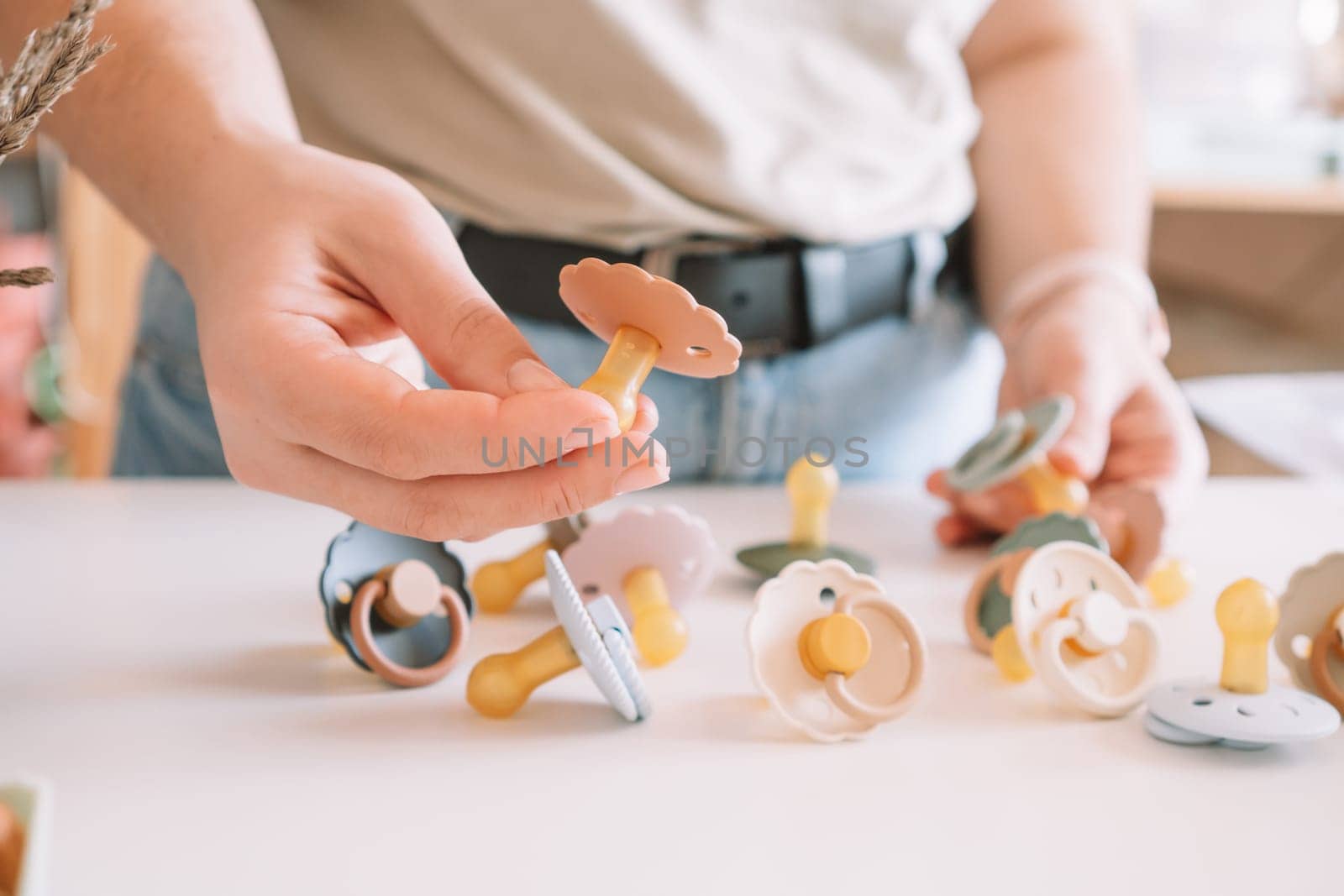 Cropped business woman hands, making and design craft silicone pacifiers for newborn babies on white desk. Small business, store. Choosing soft material for kids. Natural ecological accessories.