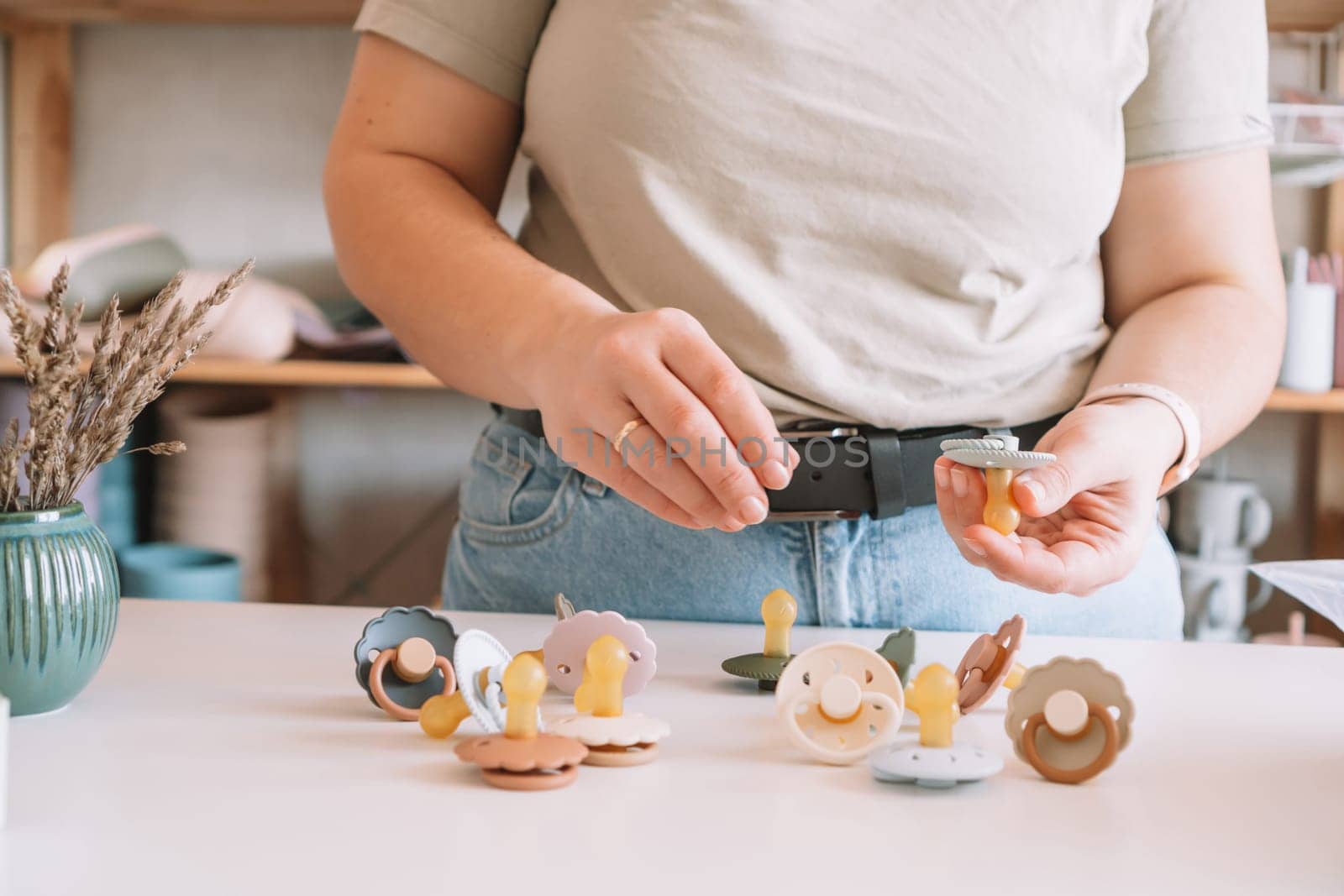 Cropped business woman hands, making and design craft silicone pacifiers for newborn babies on white desk. Small business, store. Choosing soft material for kids. Natural ecological accessories.