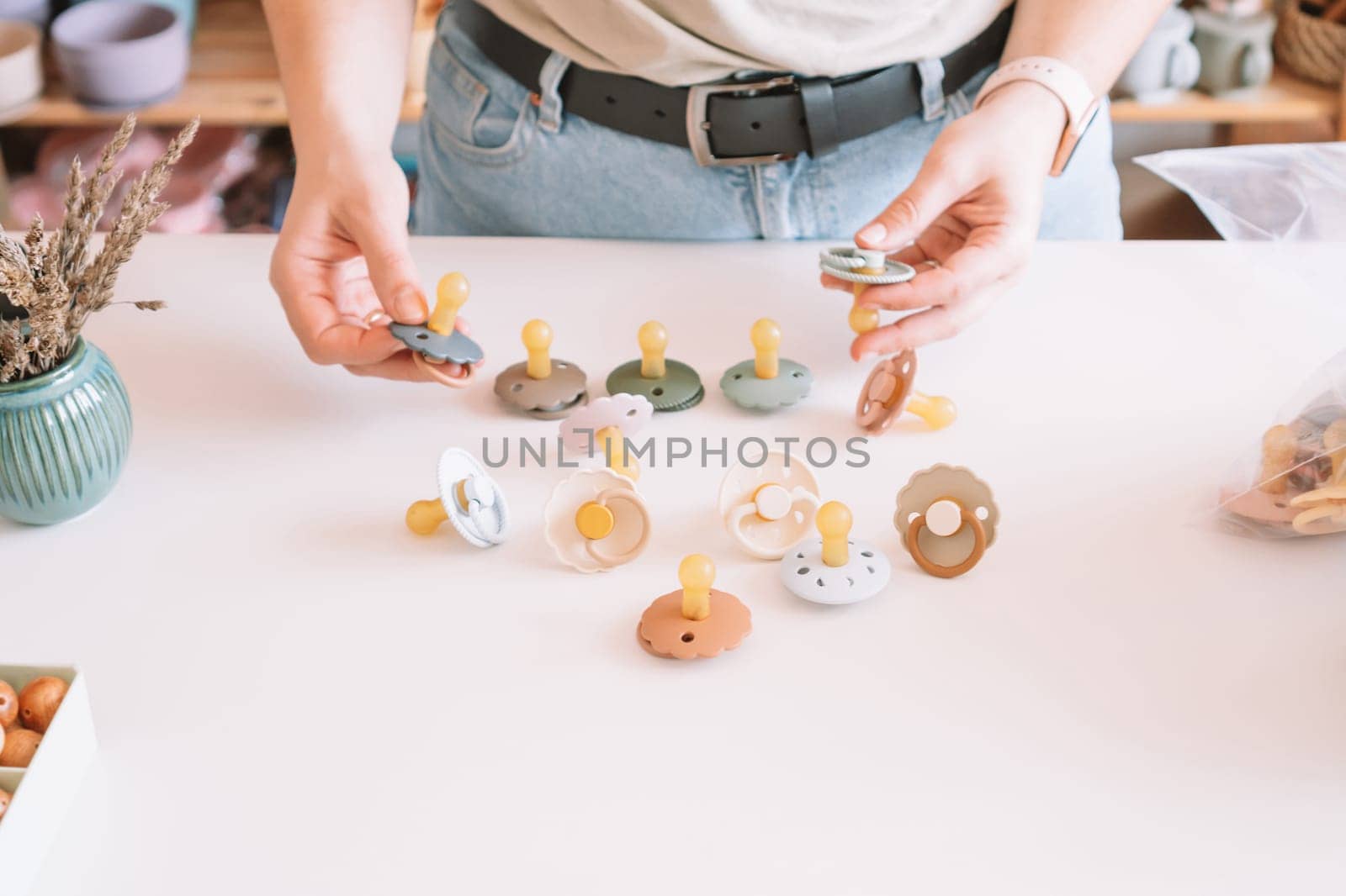 Cropped business woman hands, making and design craft silicone pacifiers for newborn babies on white desk. Small business, store. Choosing soft material for kids. Natural ecological accessories.