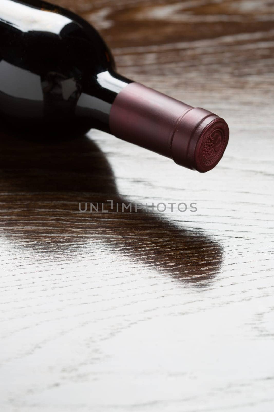 Red Wine Bottle Laying on a Wood Surface Fading Down to White.