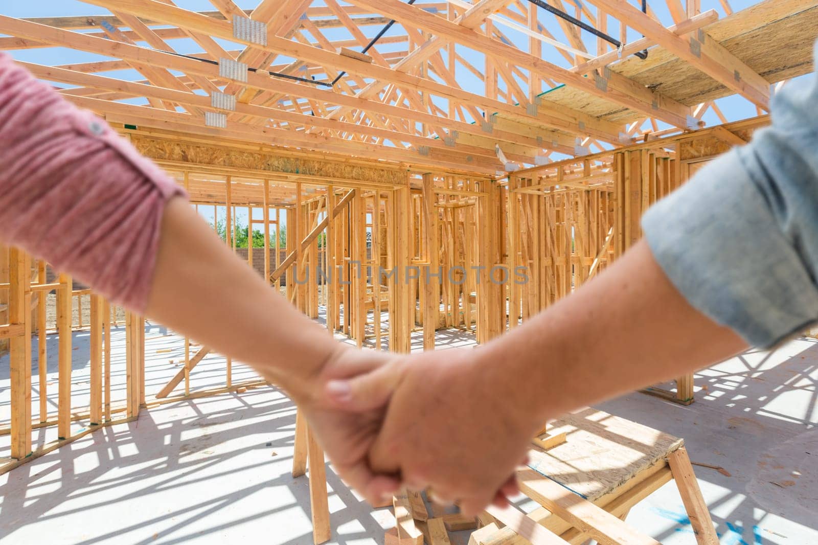 Couple Holding Hands Looking At Their New House Framing Under Construction.