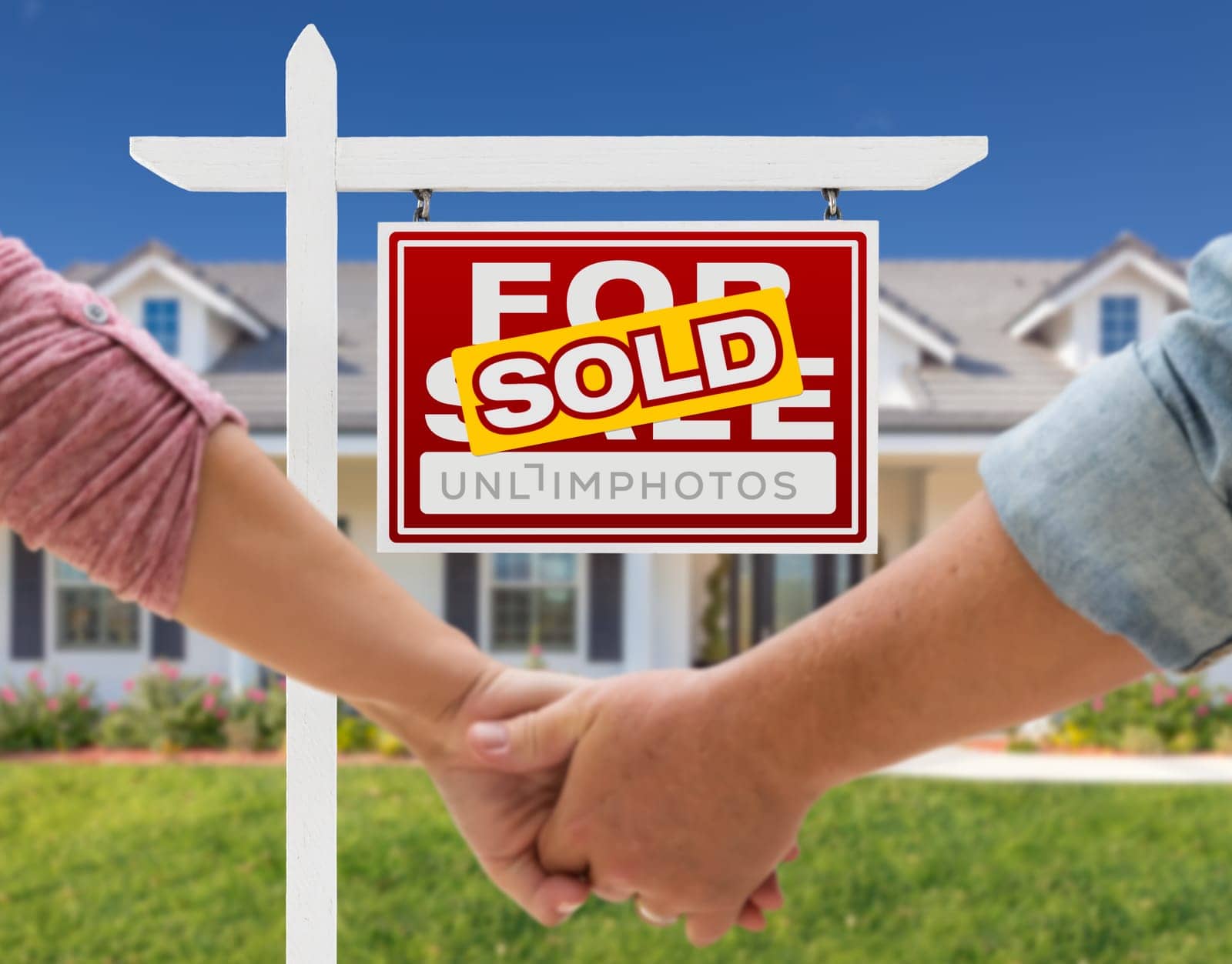 Couple Holding Hands In Front of Beautiful New House and Sold For Sale Real Estate Sign.
