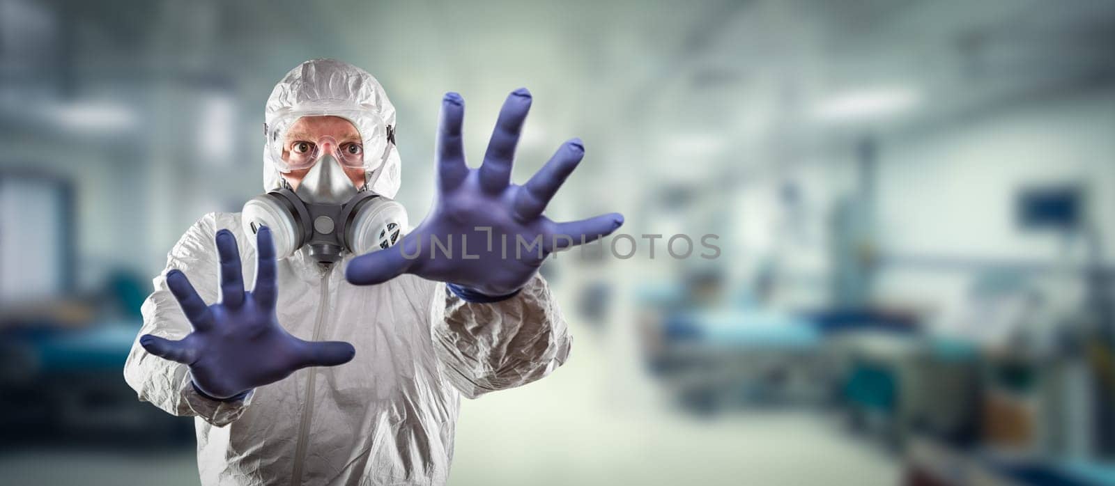 Man Wearing Hazmat Suit, Protective Gas Mask and Goggles Reaching To Stop with Hands Within Hospital.