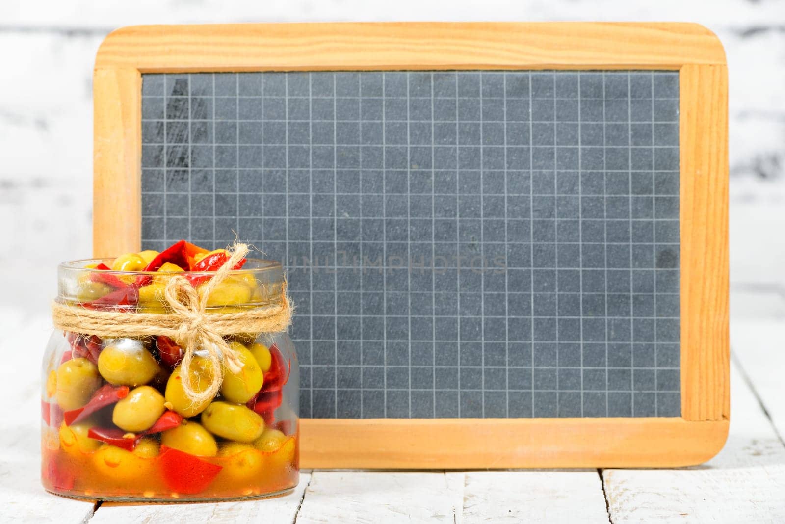 glass jar with olives and peppers with blackboard on white table