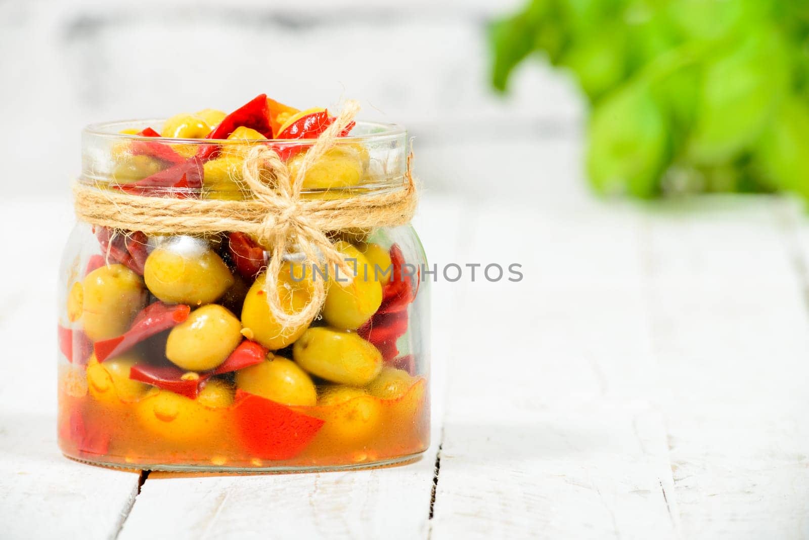 glass jar with olives and peppers on old white table