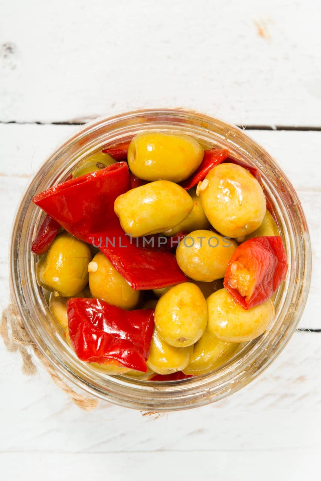glass jar with olives and peppers on old white table