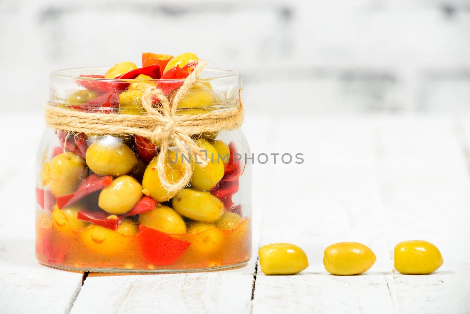 glass jar with olives and peppers on old white table