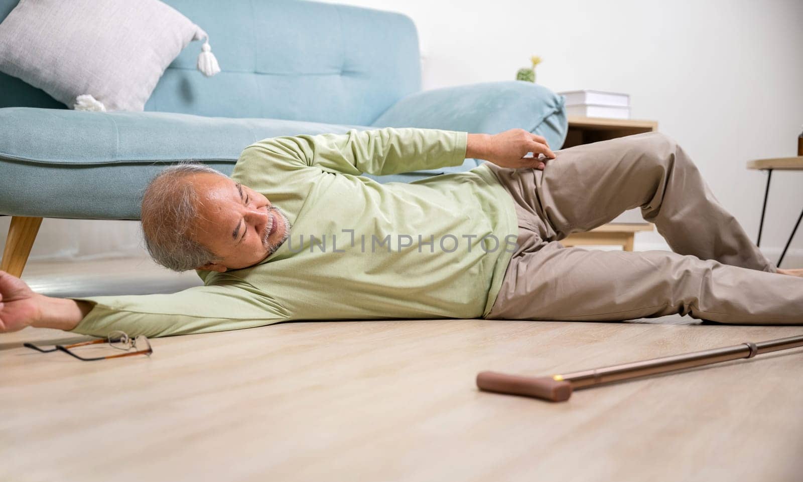 Asian old man lying on floor after falling down with wooden walking stick, Sick senior man beside couch on rug in living room at home, Elderly having an accident after doing physical therapy alone