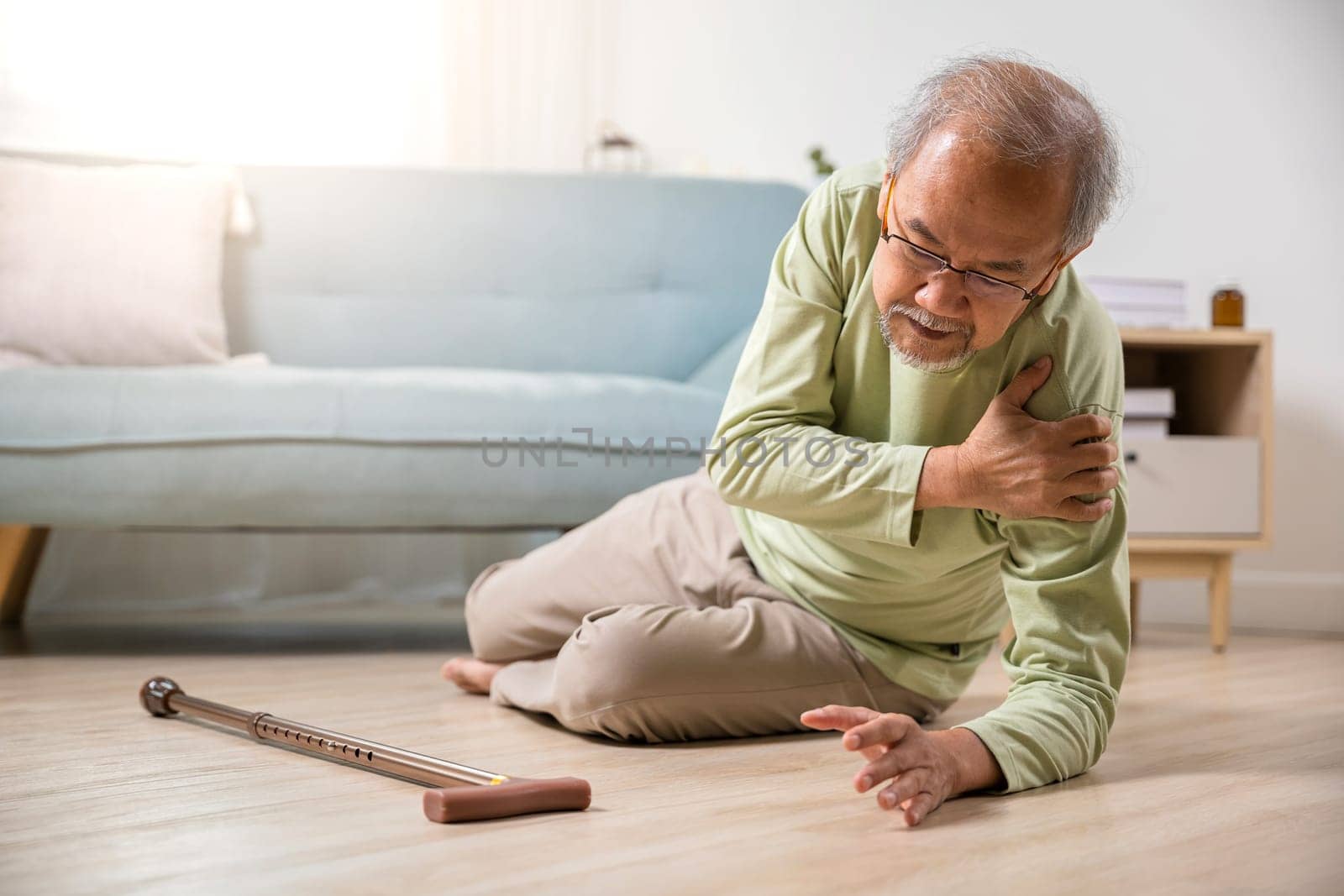 Sick senior old man falling down lying on floor because stumbled at home alone with wooden cane walking stick in living room, elderly man retired grandfather having accident after standing from sofa