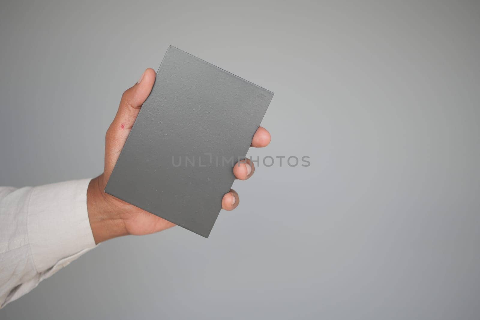 Person's hand displays a gray booklet with a simple design and color.