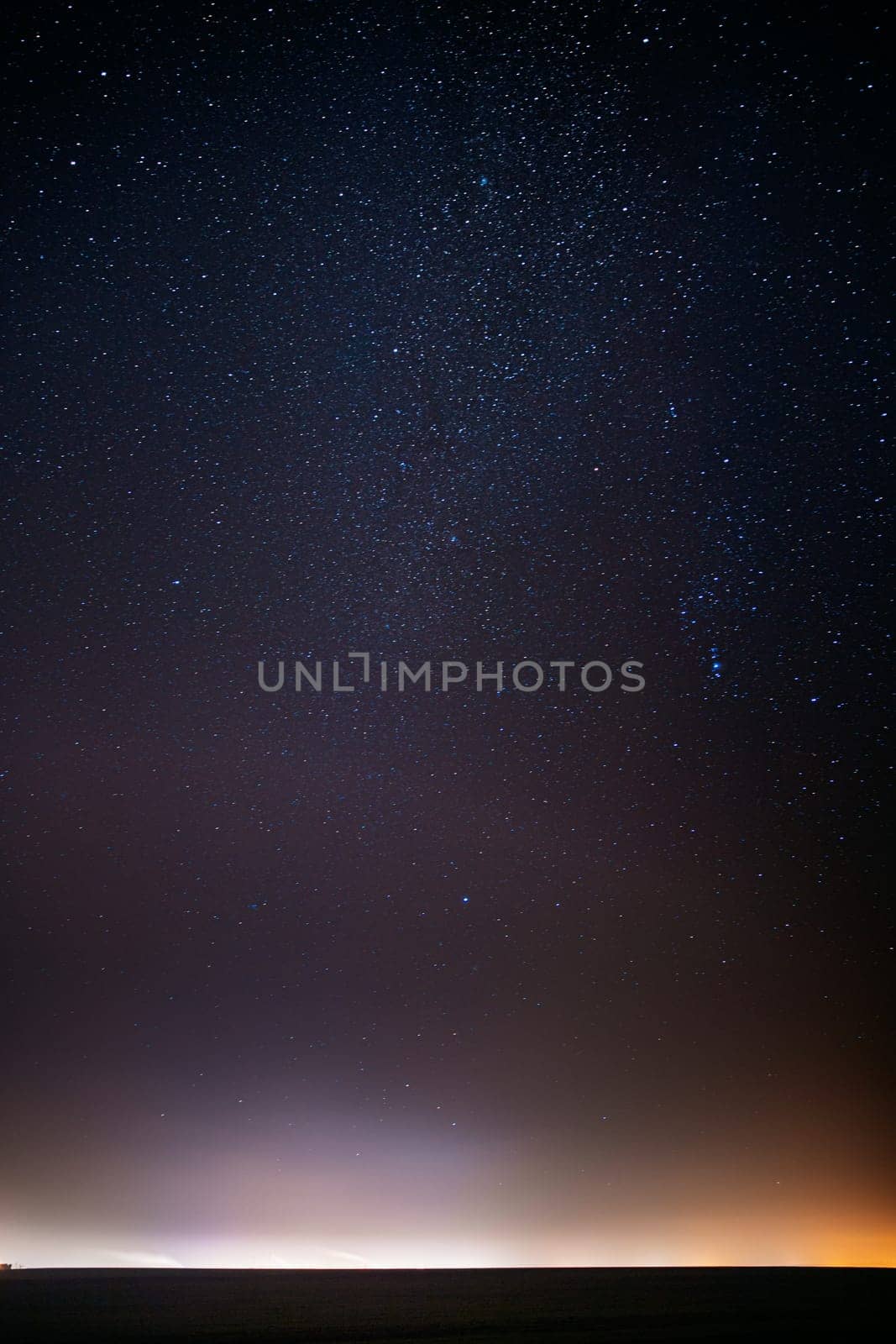 Night Starry Sky With Glowing Stars Above Countryside Landscape. Milky Way Galaxy And Rural Field Meadow In Early Spring. Bright Glowing Stars.