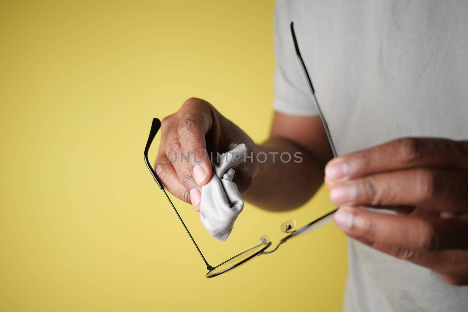 A person polishes eyeglasses with a cloth on a yellow background.