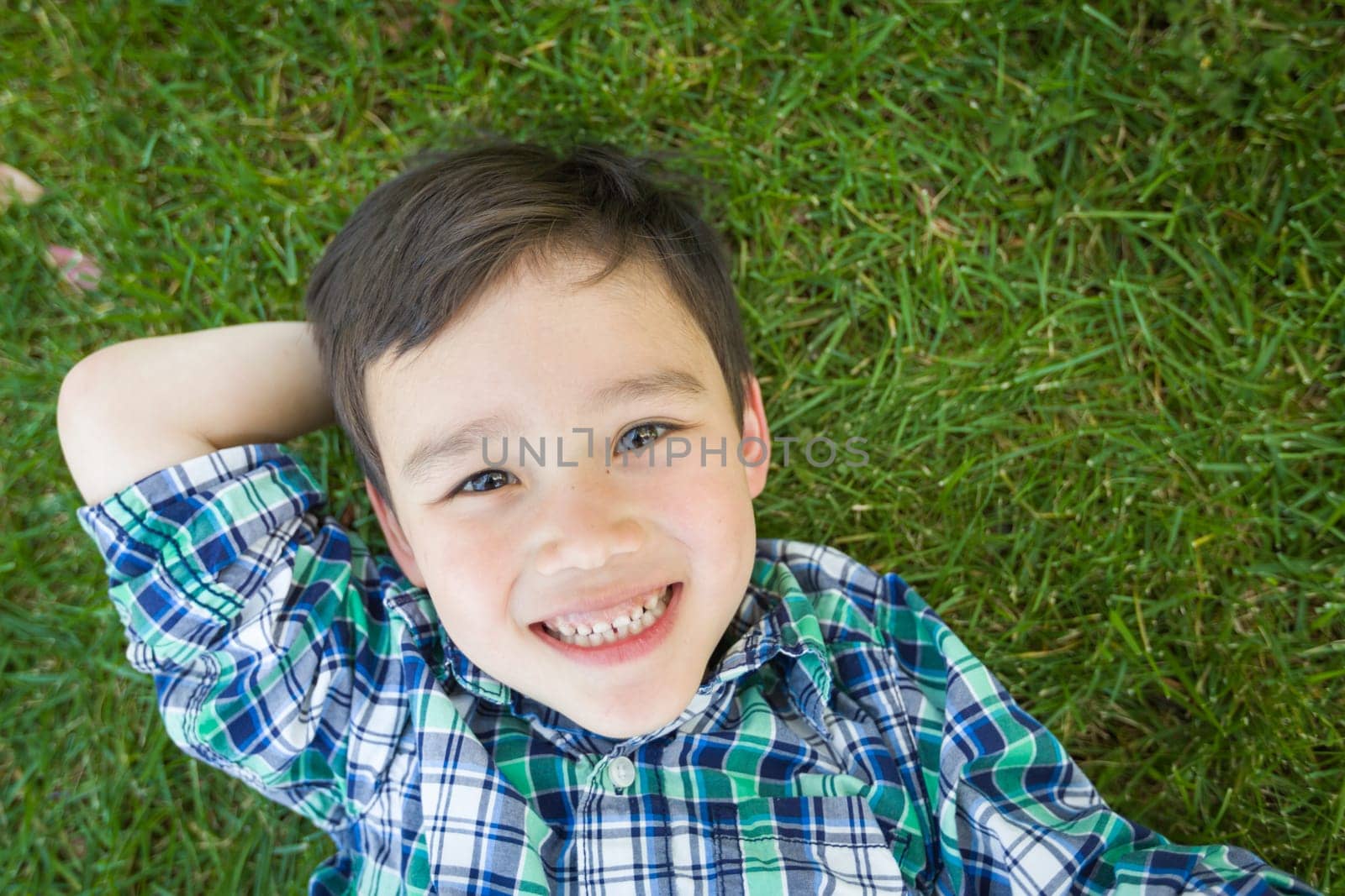Mixed Race Chinese and Caucasian Young Boy Relaxing On His Back Outside On The Grass.
