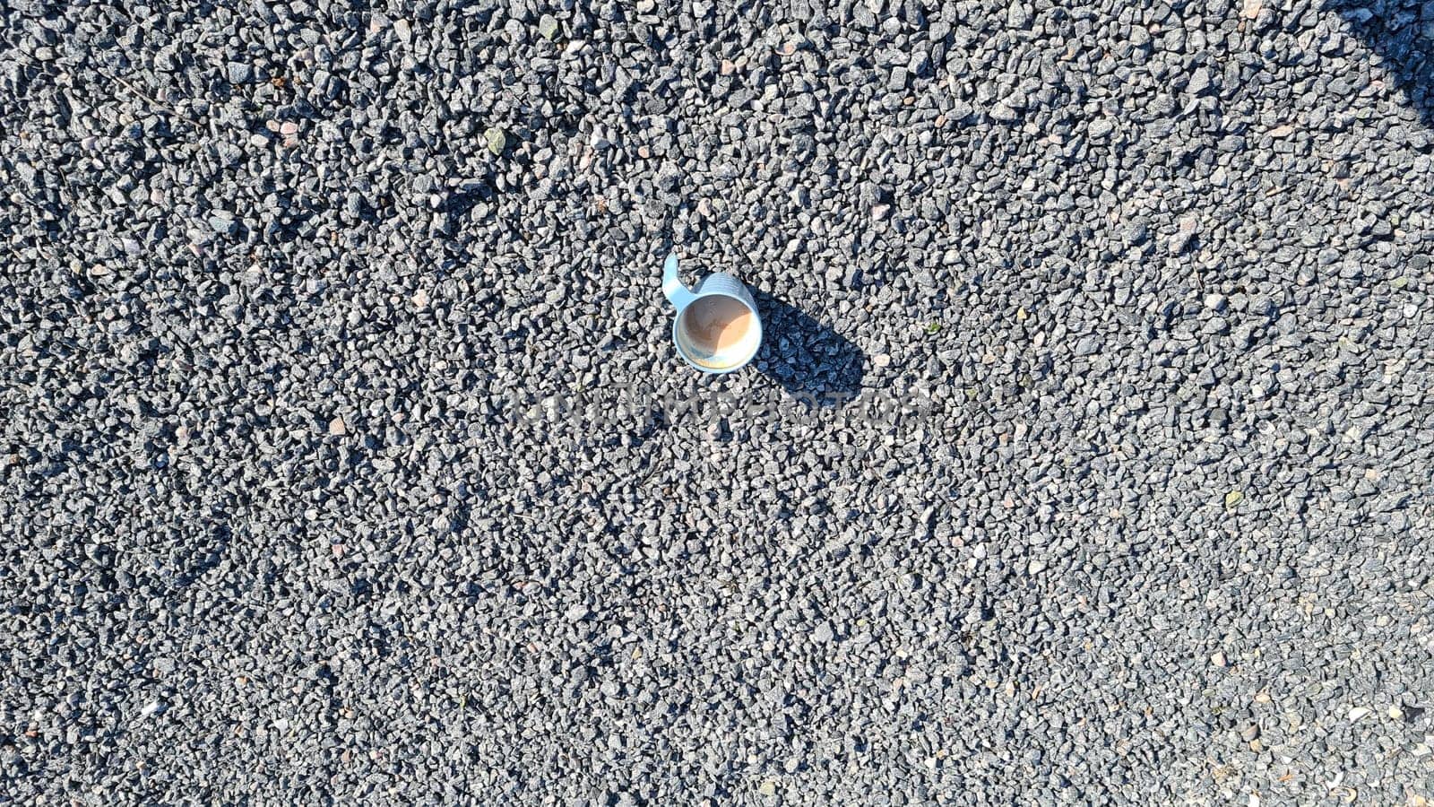 Blue coffee cup with fresh coffee stands on the floor, surrounded by small gray pebbles