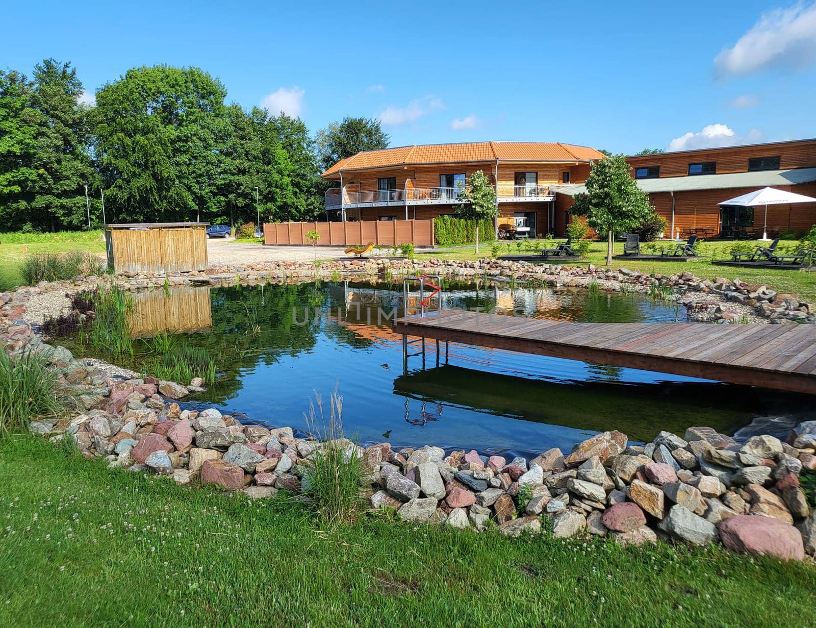 Natural pond of a natural pool with wooden bridge and entrance - natural pool in the background a country hotel