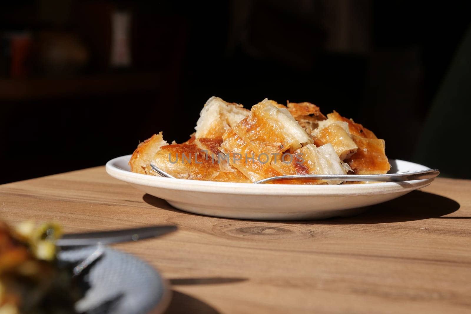 A plate of golden crispy pastries catches sunlight on a wooden table.