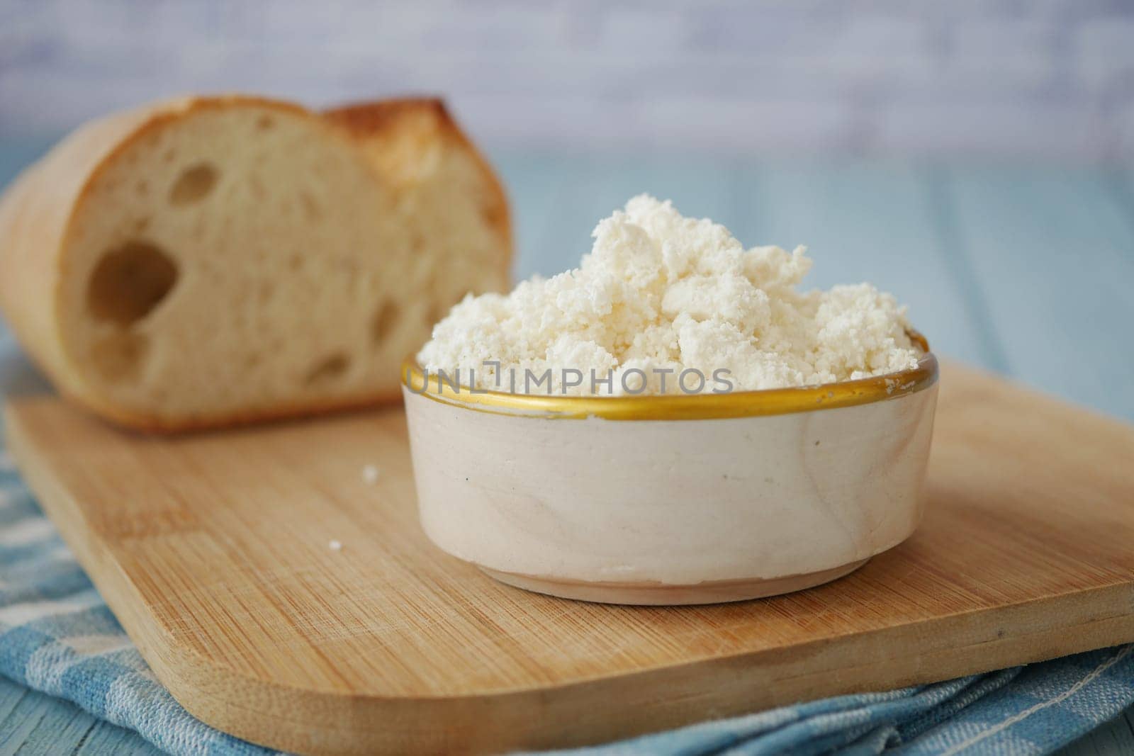 Cottage cheese served in a bowl next to fresh bread on a cutting board.