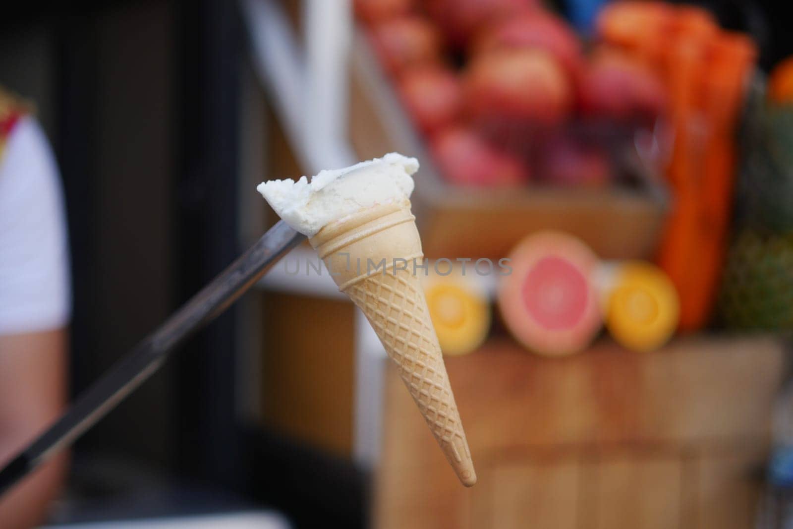 A person serves a scoop of creamy ice cream in a cone at a market.