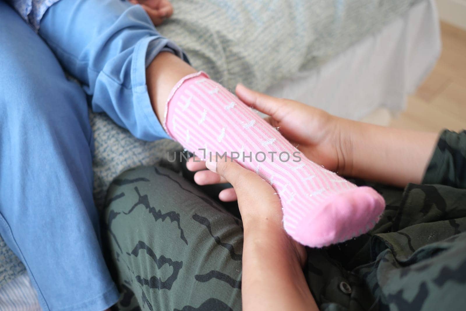 Hands assist in carefully dressing a child in soft pink socks.