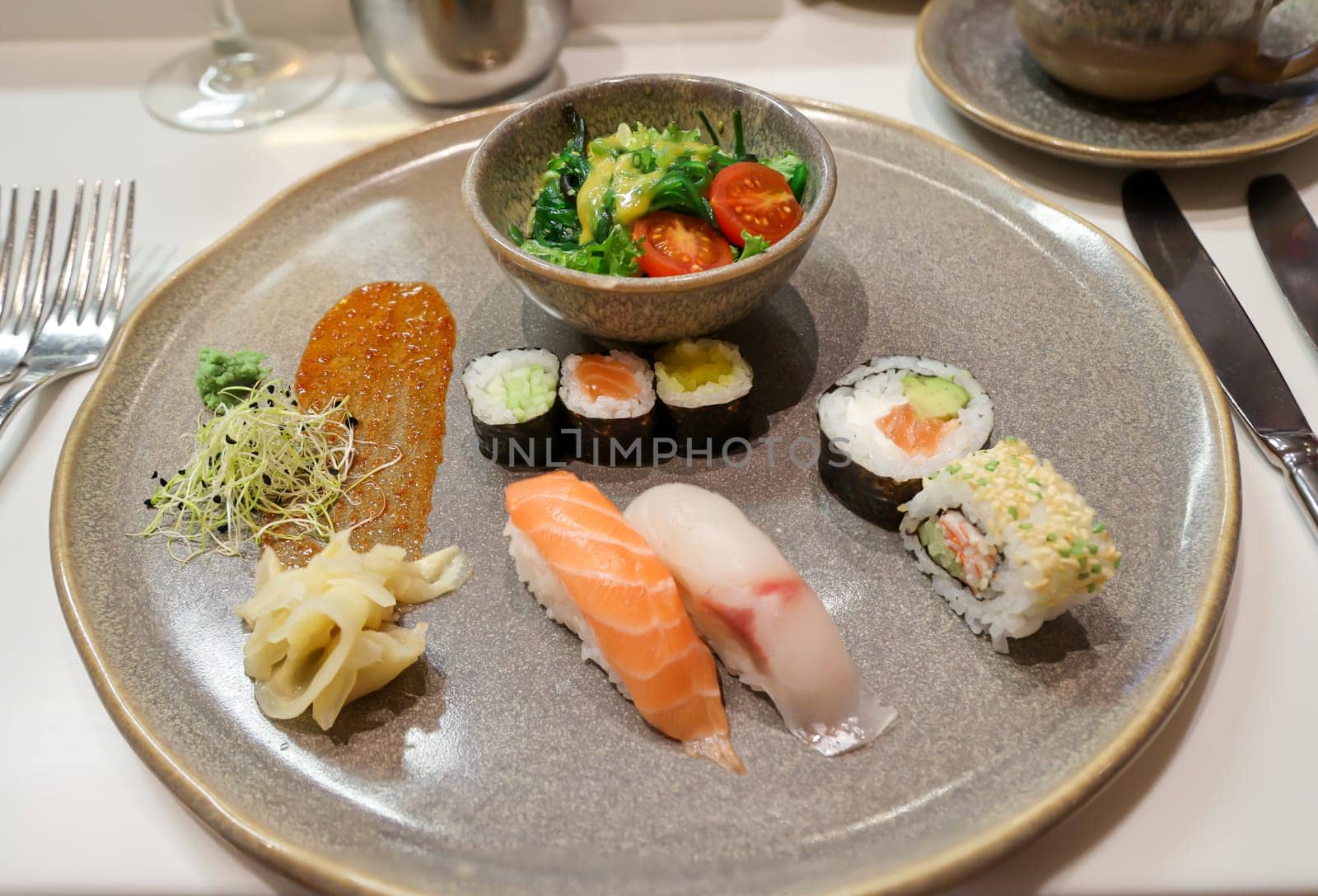 A plate of salad and sushi rolls, fresh raw fish.