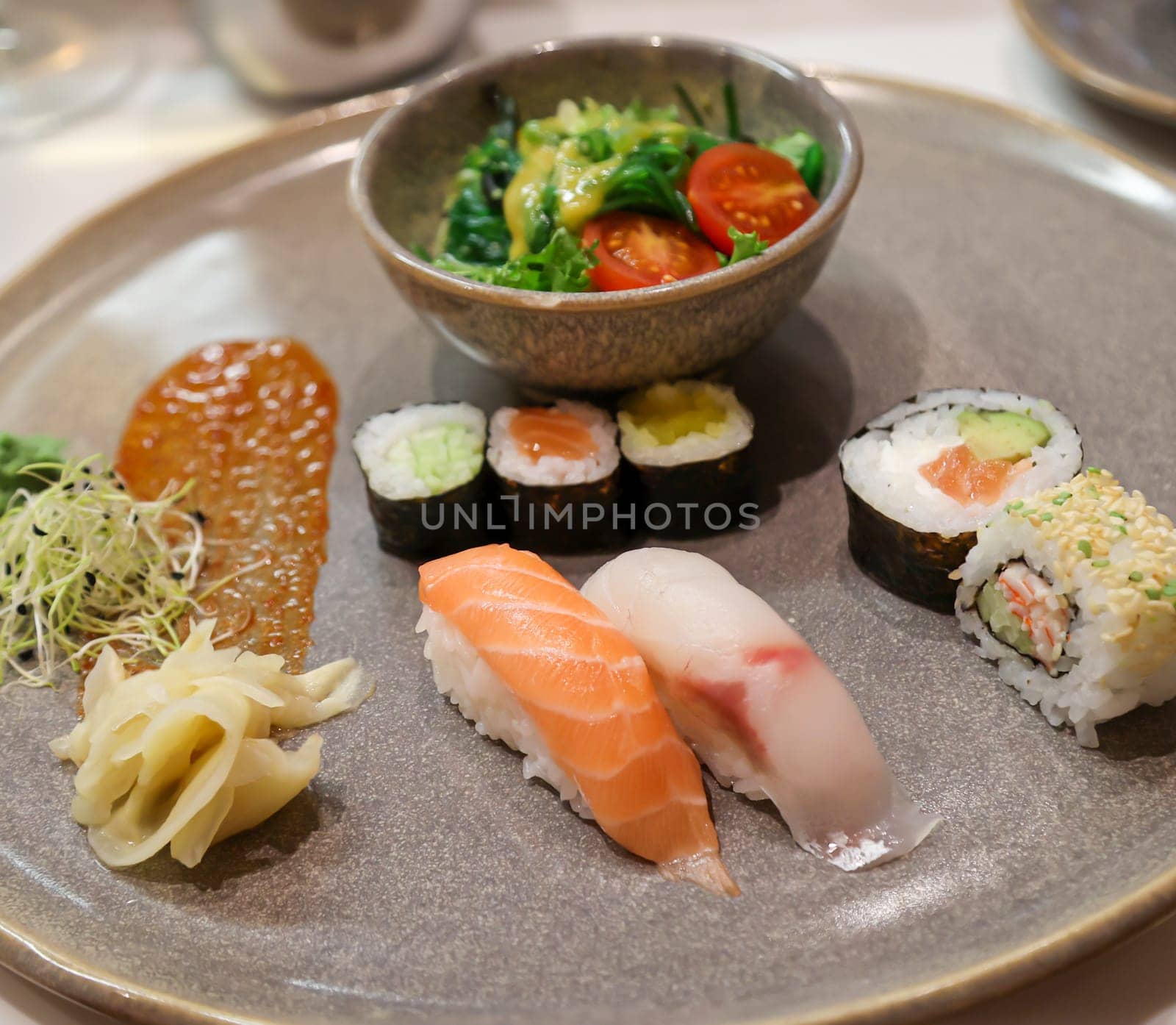 A plate of salad and sushi rolls, fresh raw fish.