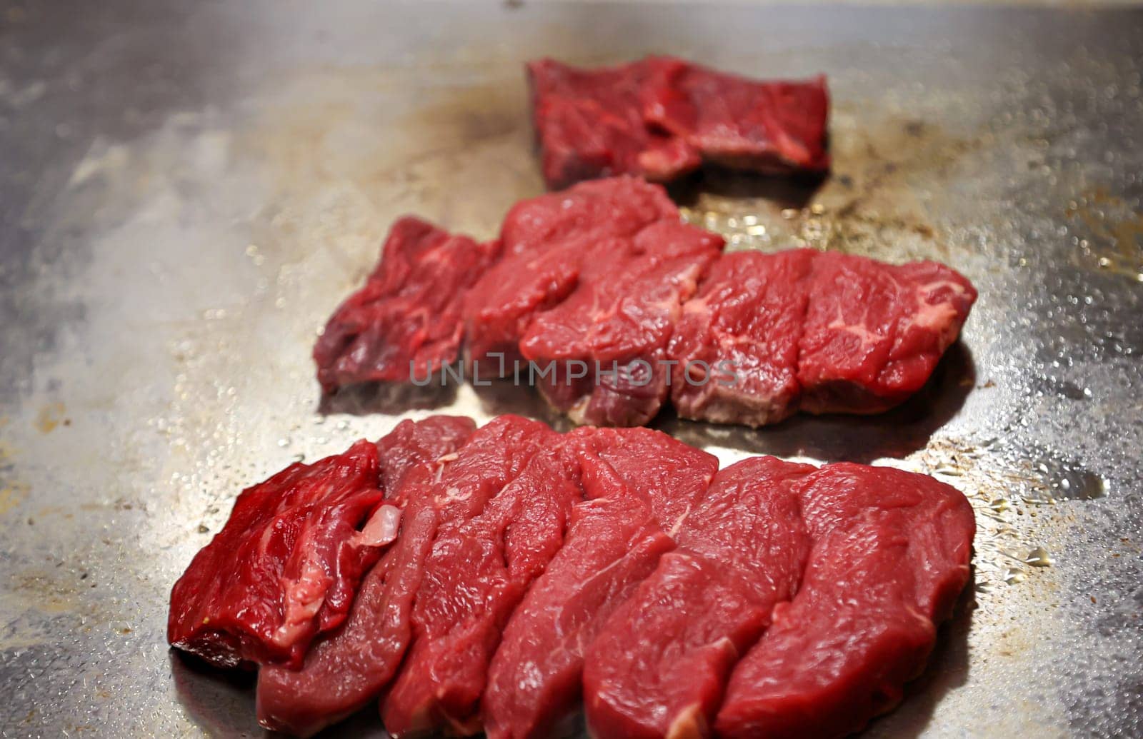 Still raw beef lies on a hot surface for frying.
