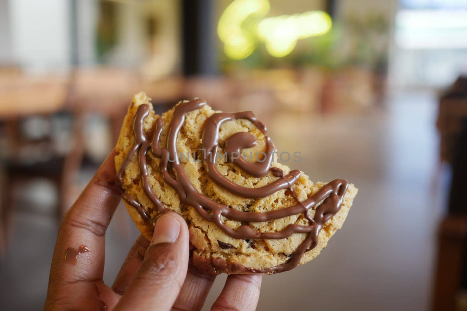 A person enjoys a chocolate-swirled cookie at a warm, inviting cafe.