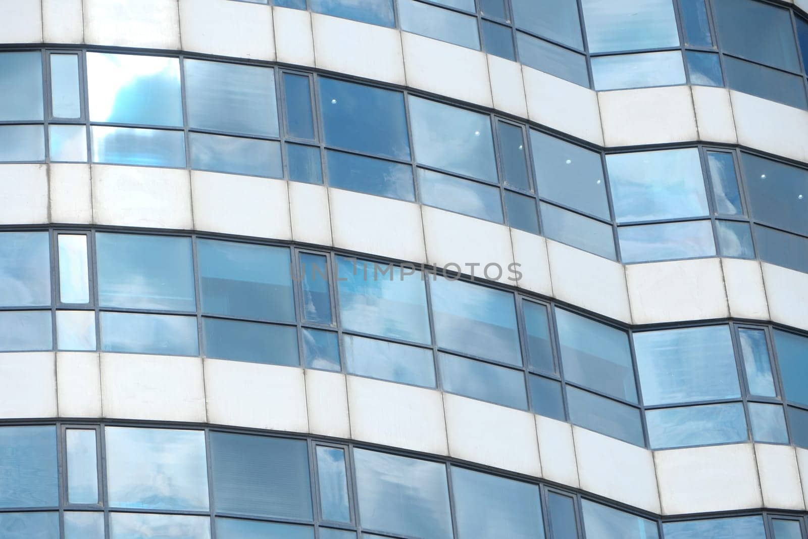 Curved glass windows of a modern building reflect clouds and light.