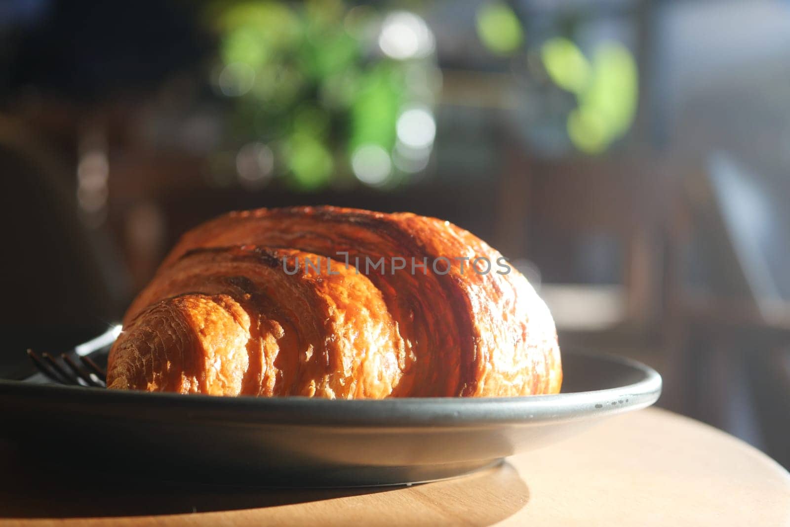 Freshly baked croissant on a dark plate in a warm cafe atmosphere.