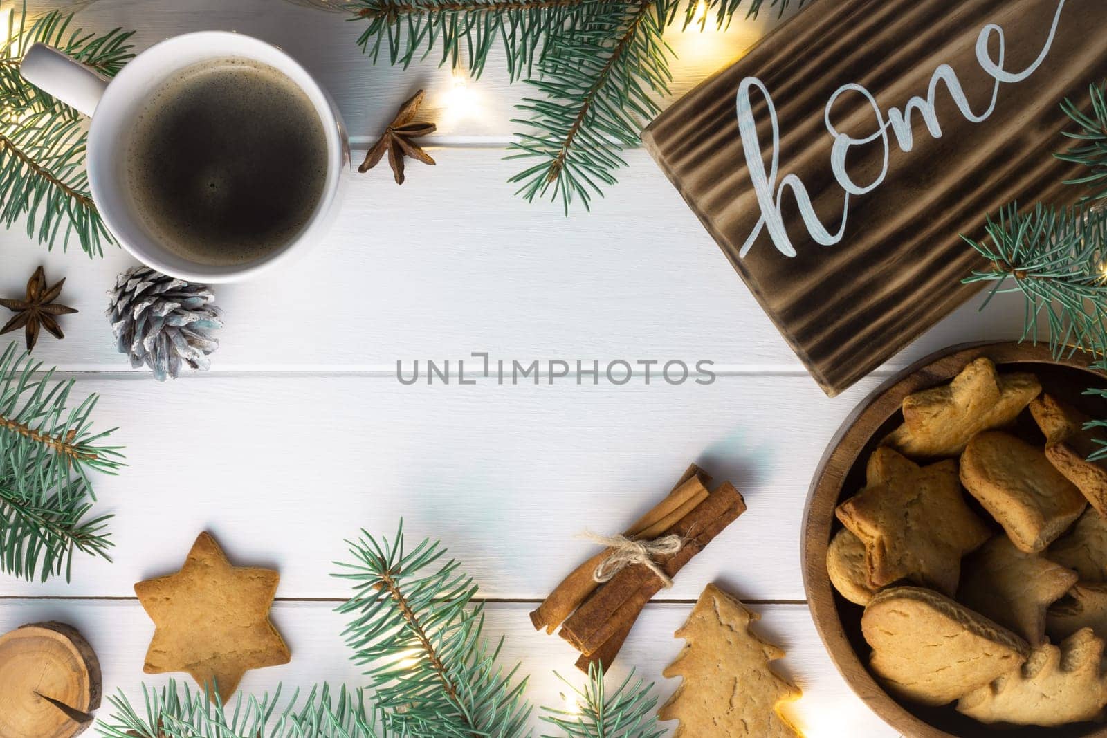 Home lettering burnt wood sign, gingerbread cookie, Christmas tree branches, cup of coffee, cinnamon sticks on white surface. Flat lay. Copy space.