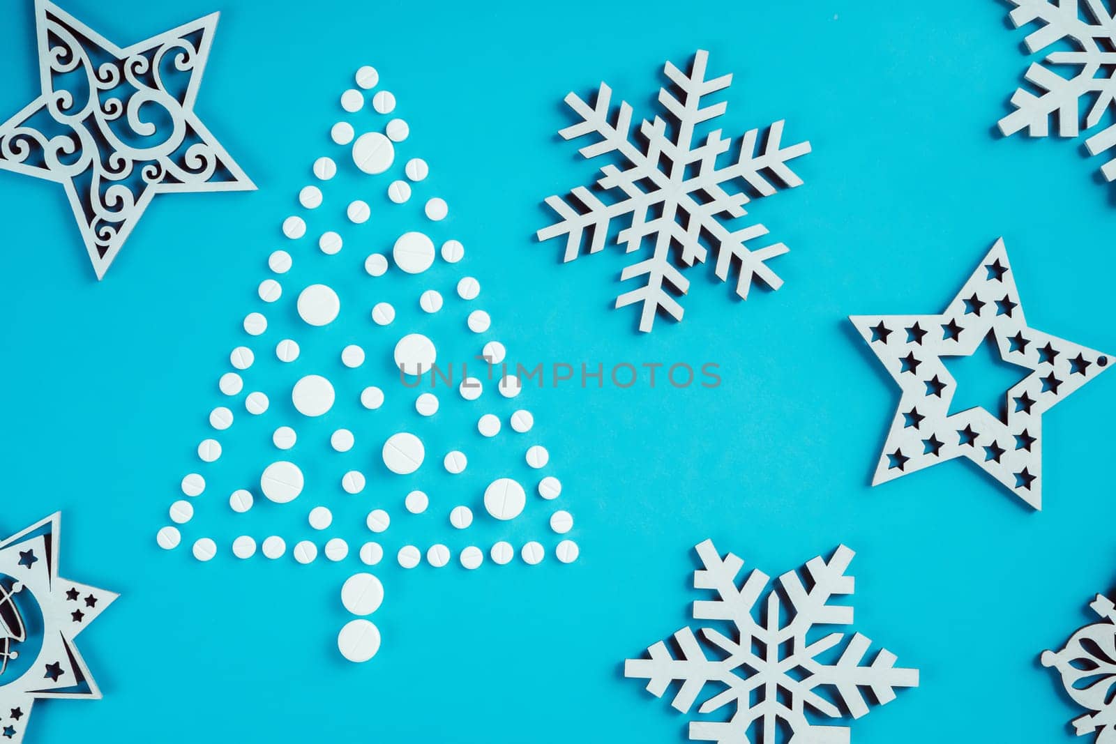 White round pills, laid out in shape of Christmas tree with wooden snowflakes on light blue background. Flat lay