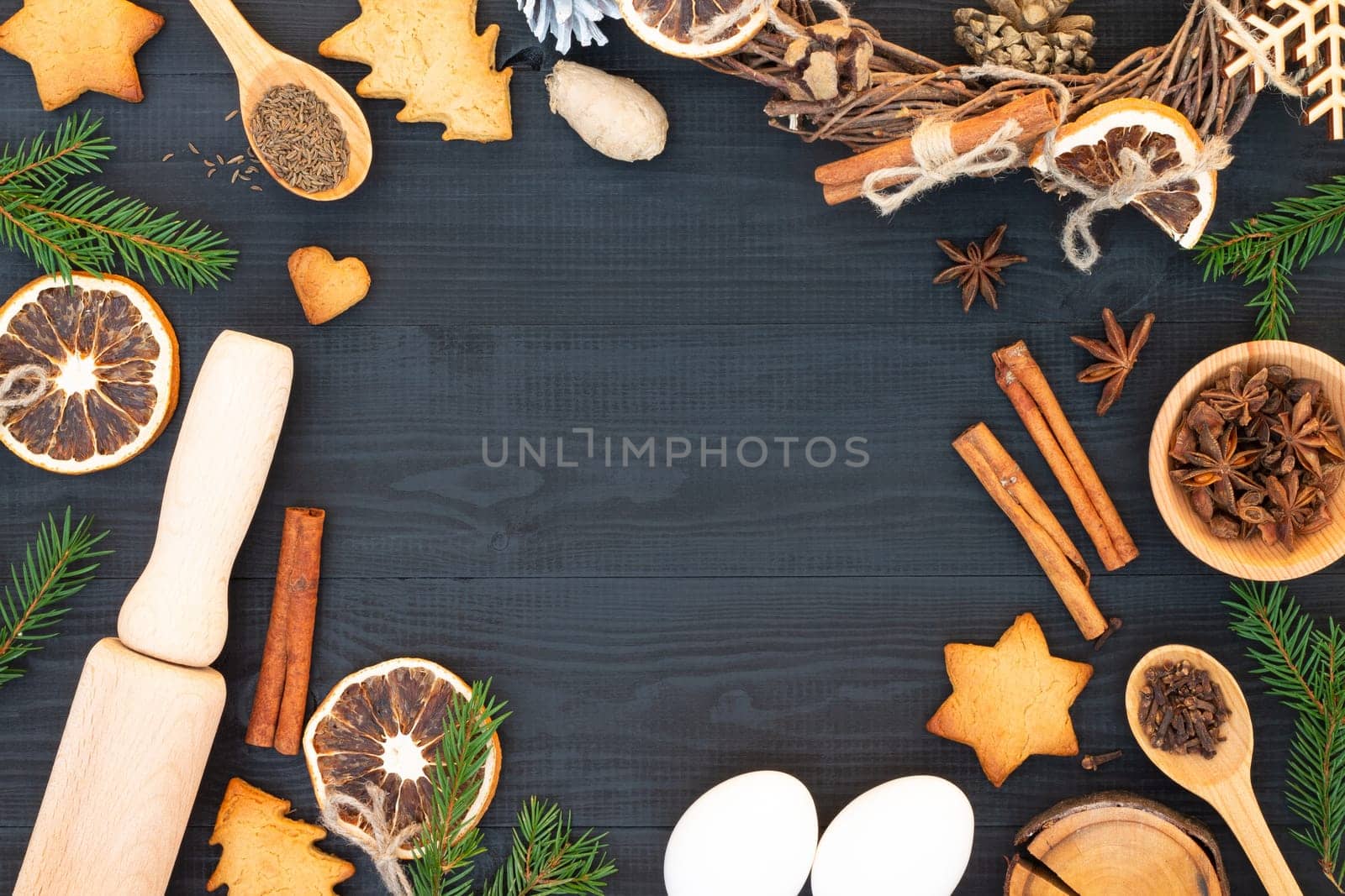Christmas tree branches, gingerbread cookies, spices and baking supplies on black wood background. Christmas, New Year greeting card