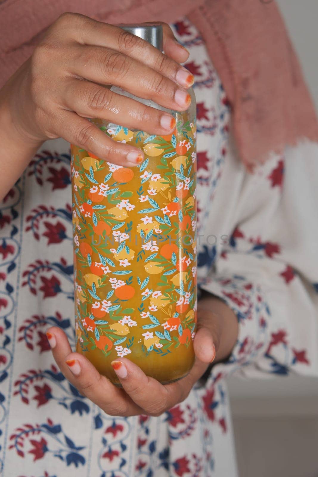 A person holds a vibrant beverage bottle decorated with flowers.