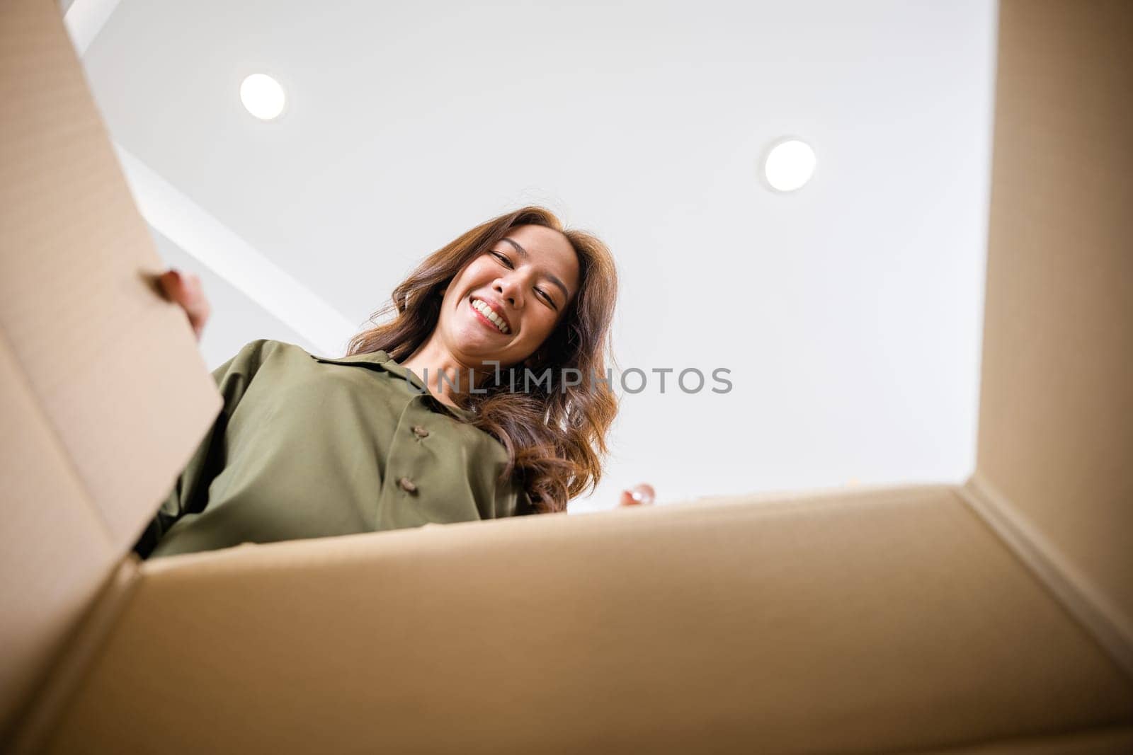 Happy Asian young woman opening carton box from internet store order shopping online at home, Smiling female surprised unpacking christmas gift big box and looking inside, inside bottom view