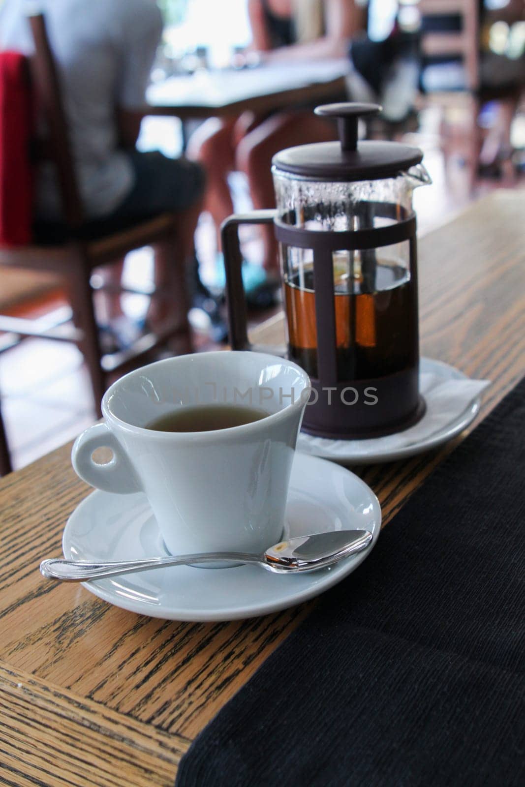 White cup of tea with glass teapot behind on wood table in small cozy cafe