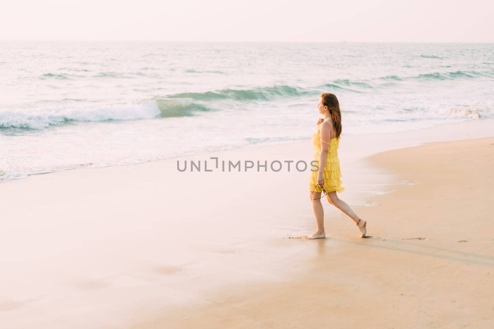 Goa, India. Young Caucasian Woman In Yellow Dress Go To Sea Ocean And Looking Into Distance.