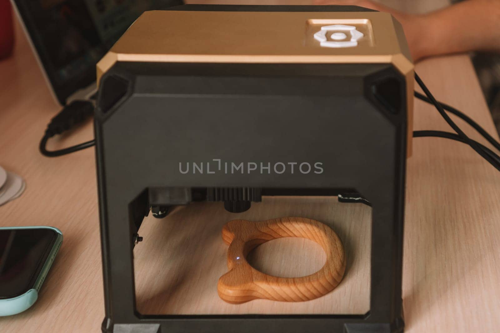 Desktop laser wood burning machine uses a blue laser beam to inscribe name on surface of childrens wooden toy. Home production of teethers and rattles for babies