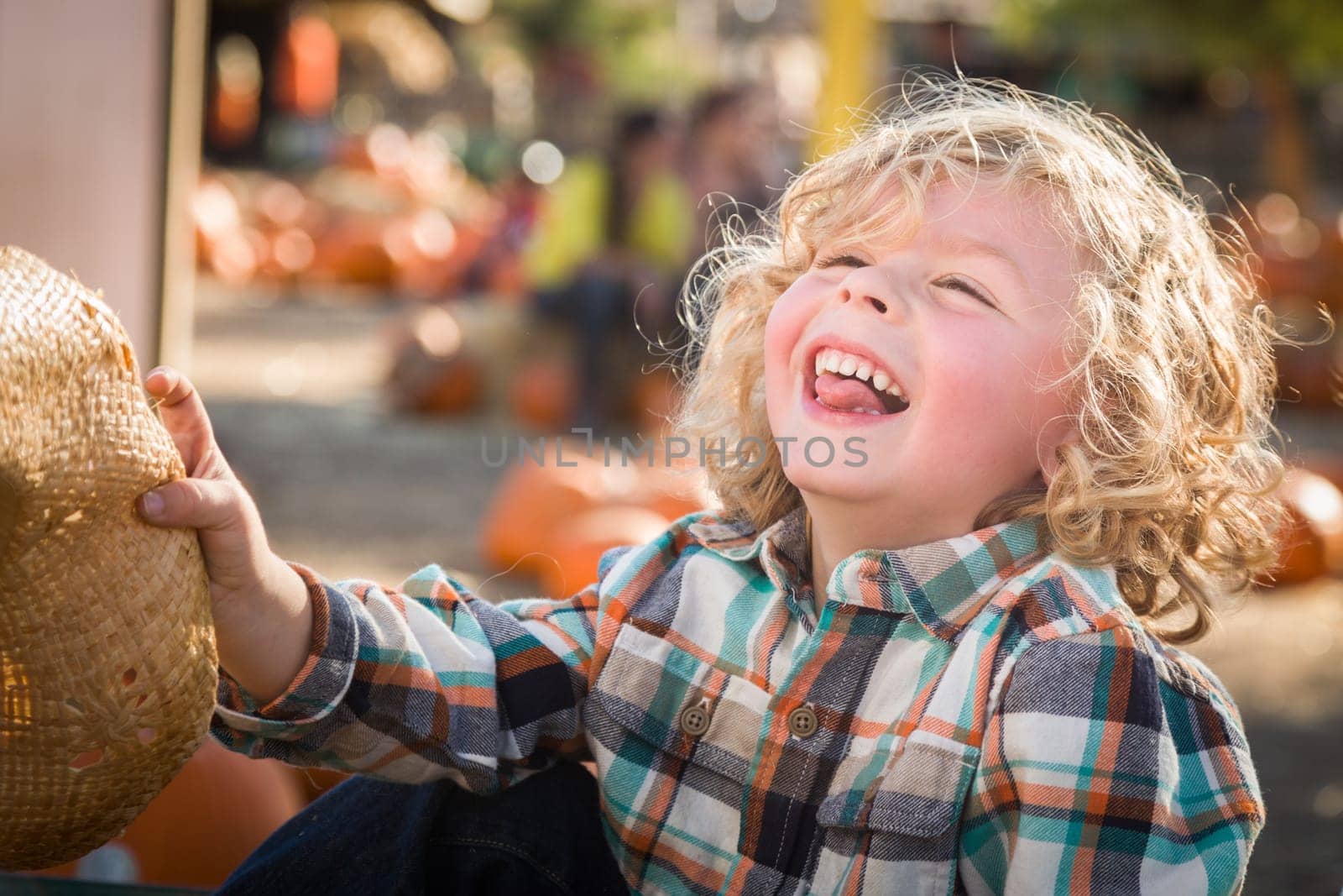 Little Boy Sitting With A Cowboy Hat in a Rustic Ranch Setting at the Pumpkin Patch.