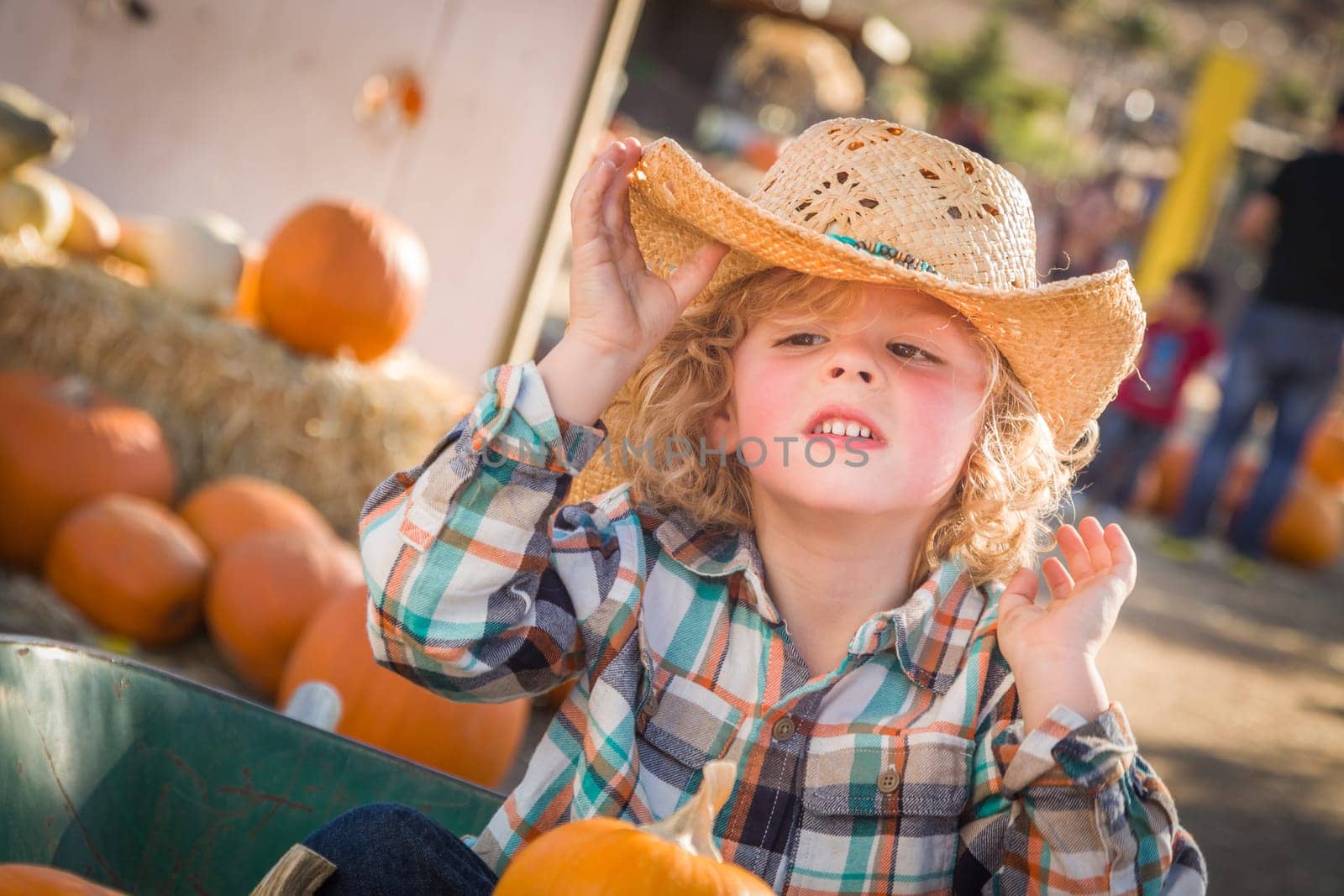 Little Boy Sitting With A Cowboy Hat in a Rustic Ranch Setting at the Pumpkin Patch.