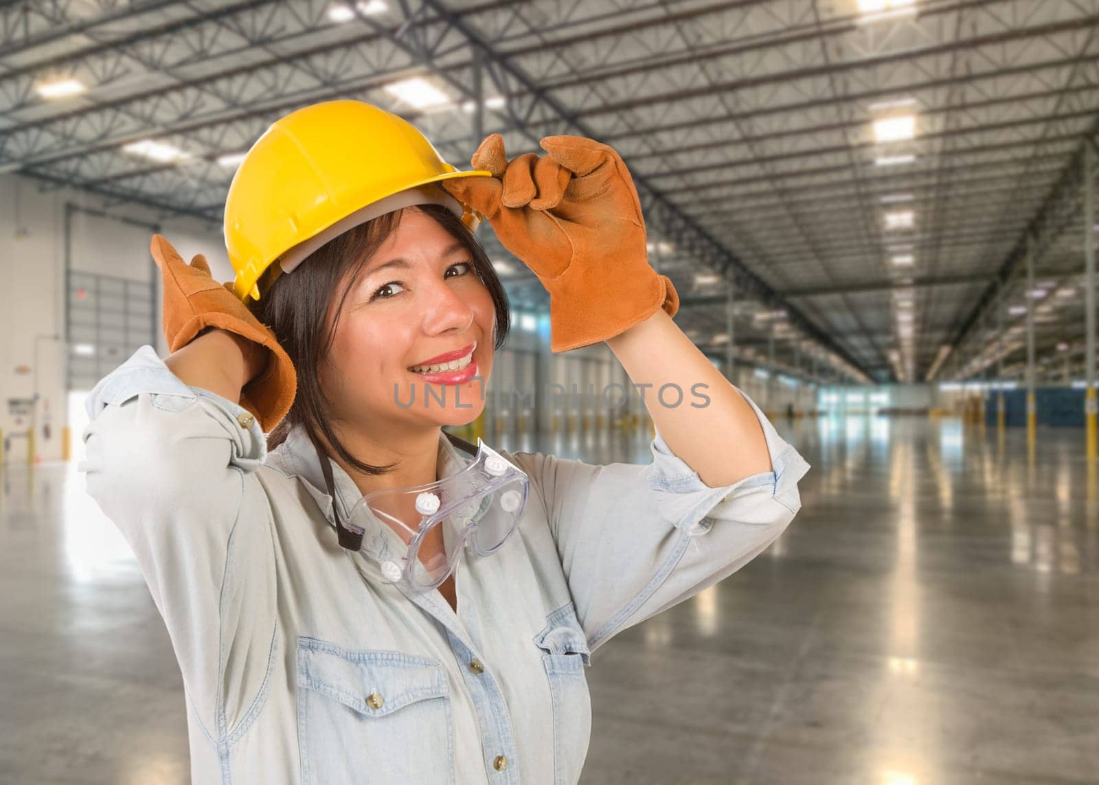Hispanic Female Contractor Wearing Hard Hat Standing in Empty Industrial Warehouse.