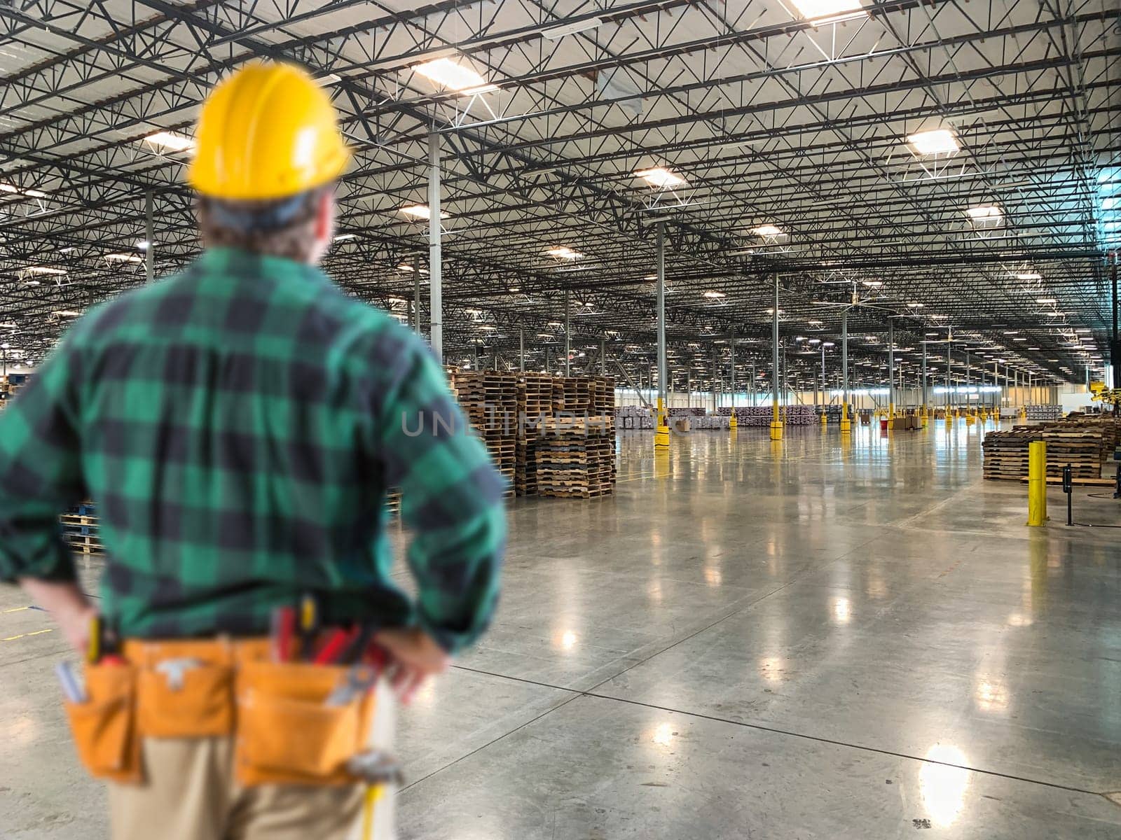 Male Contractor Wearing Hard Hat Standing in Empty Industrial Warehouse.